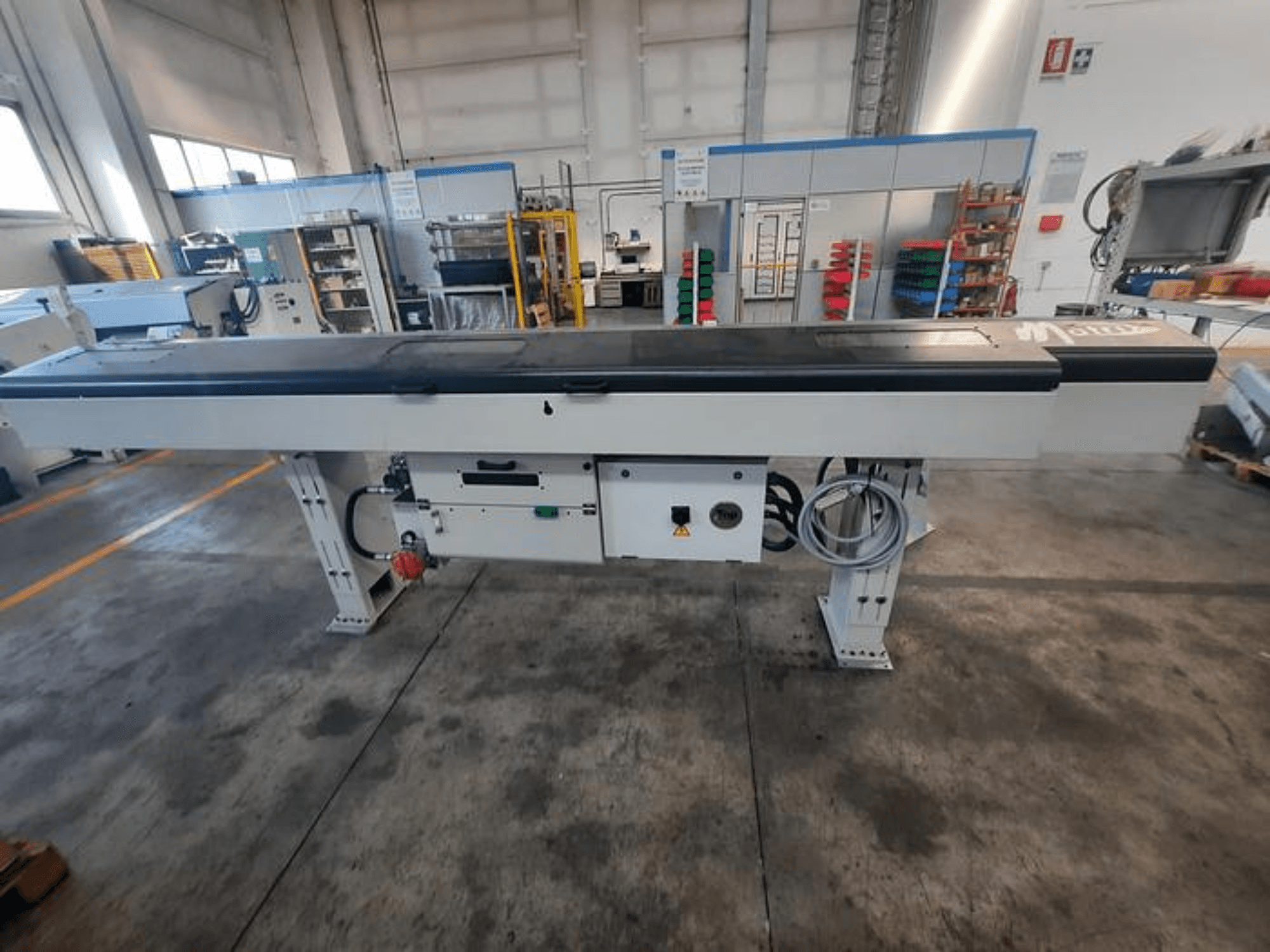 Metalni transportni stol s glatkom crnom pločom, bočni pogled, s kontrolnim tipkama i kabelima; djelomično vidljiv logotip marke.