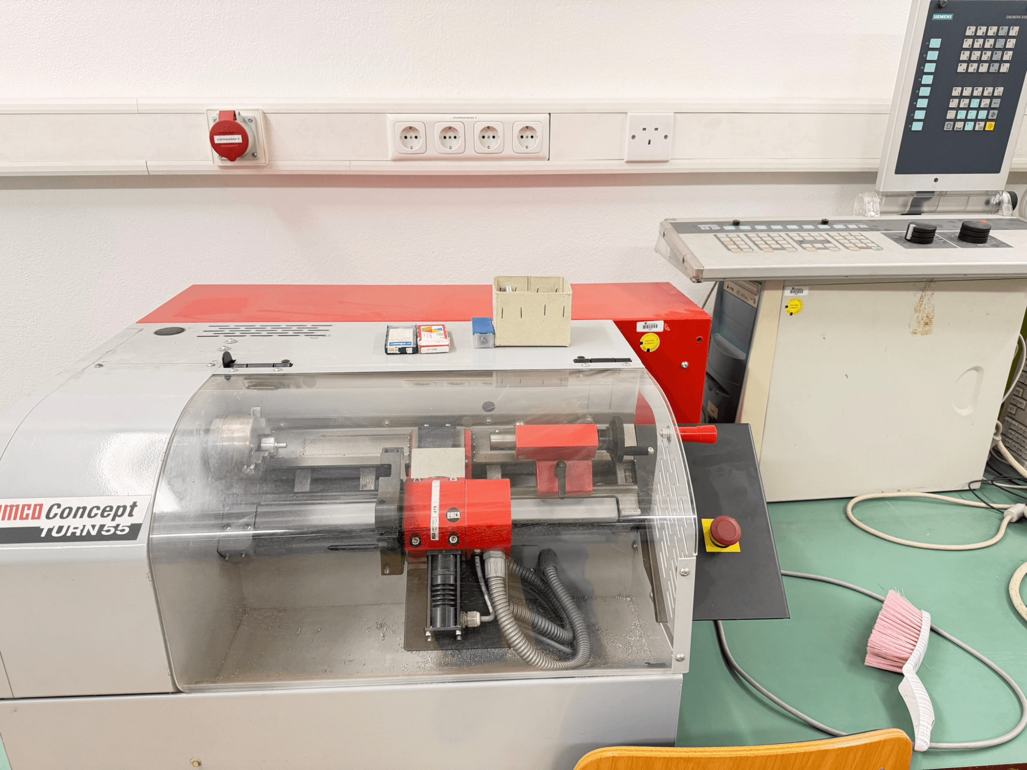 Horizontalni tokarski stroj EMCO Concept Turn 55 s crvenom i sivom vanjštinom, prednji pogled koji prikazuje kontrole i radno područje.
