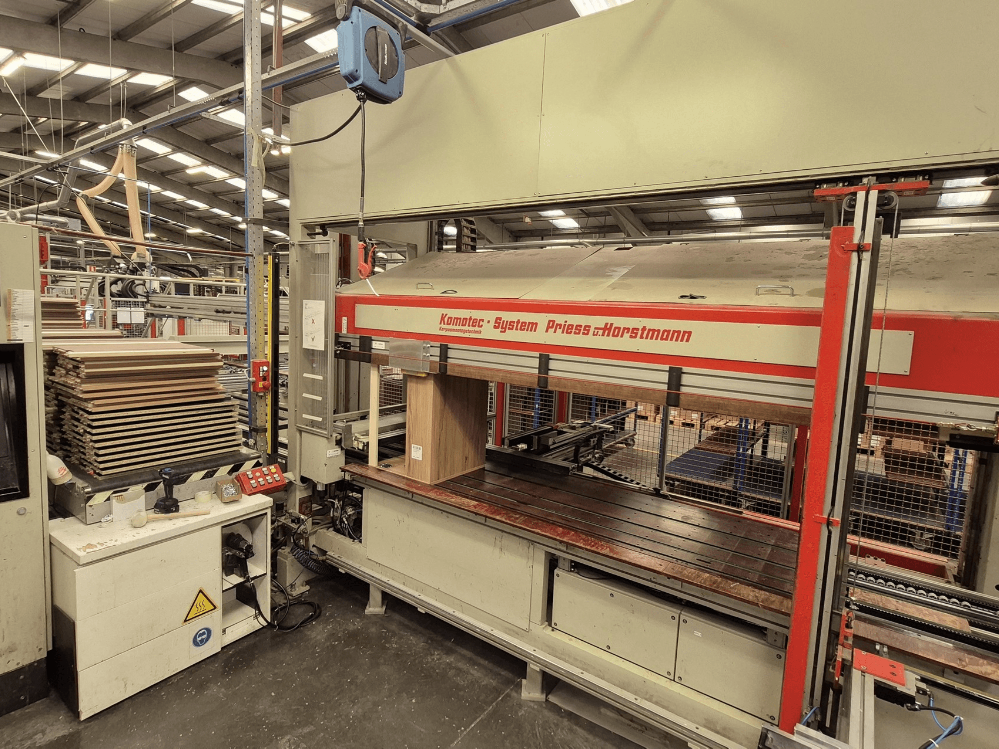 Preša za furnir KP-5-CNC tvrtke PREISS U HORTSTMANN, pogled sprijeda, prikazuje složene listove furnira i upravljačku ploču.