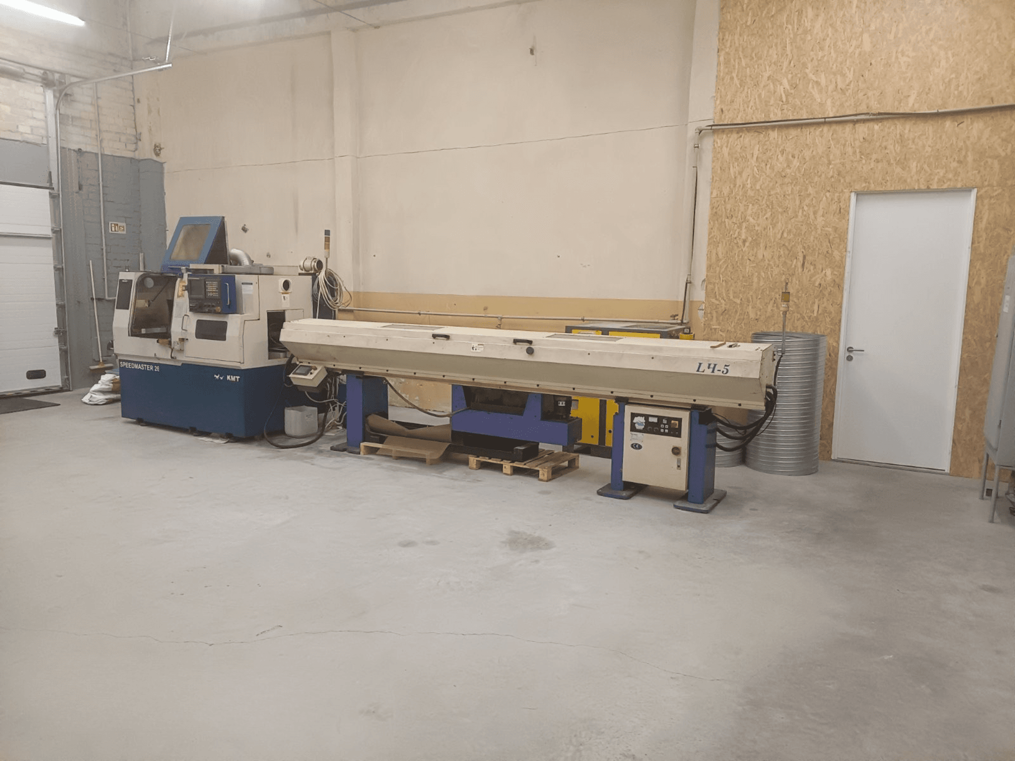 Industrijska radionica sa strojem KMT Speedmaster 34 i L4.5, gledano sprijeda, s vidljivim upravljačkim elementima i strojevima.
