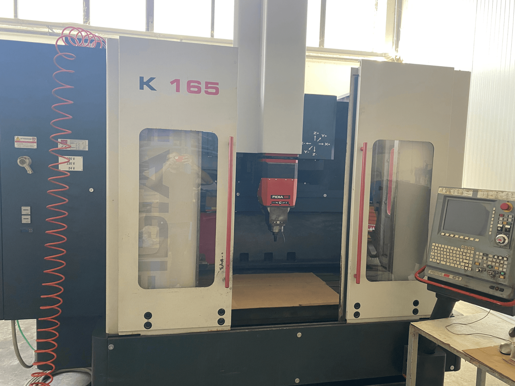 Fidia K 165 CNC stroj s crvenim vretenom i upravljačkom pločom, gledano sprijeda, u dobro osvijetljenom okruženju radionice.