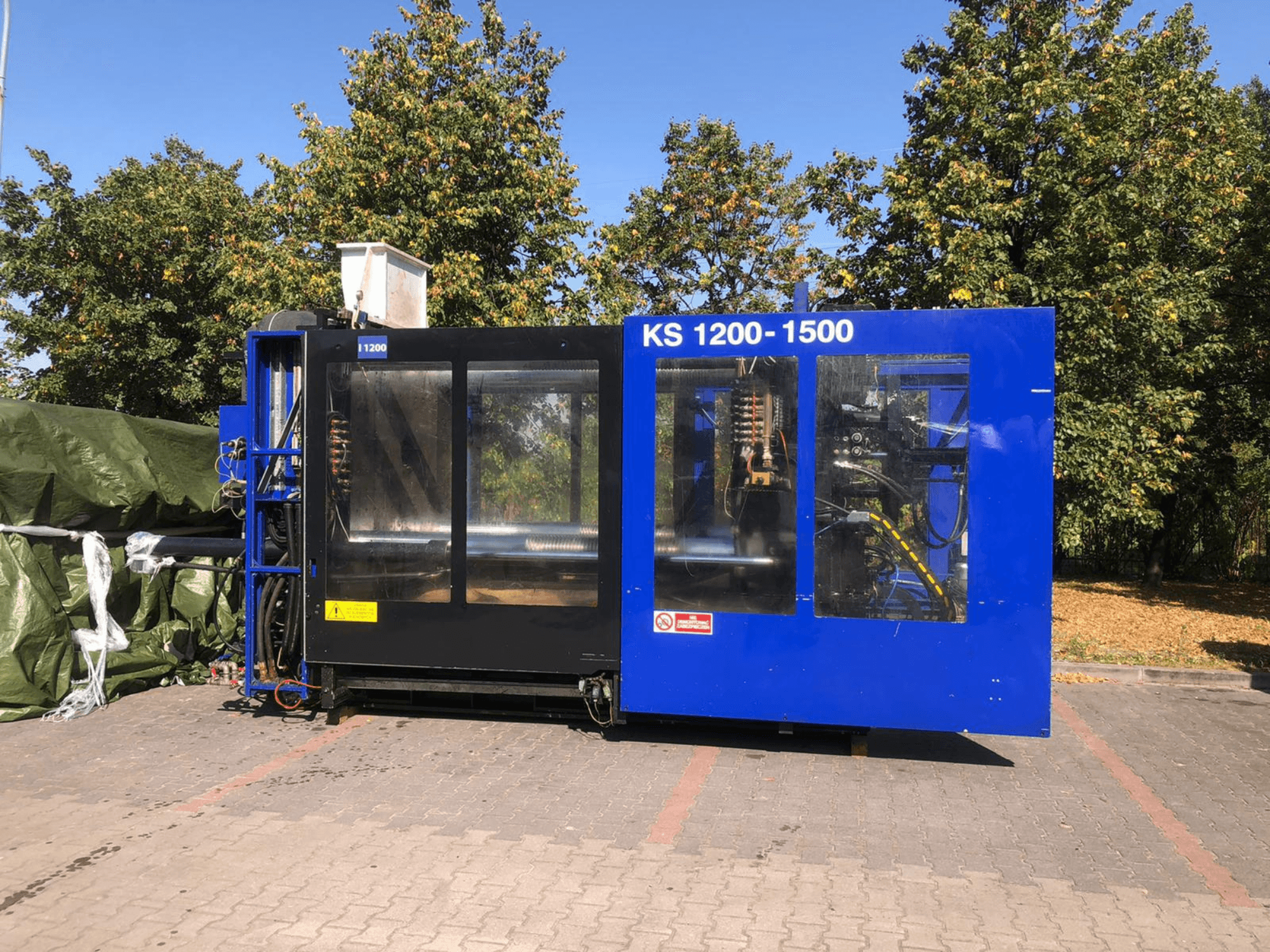 Hidraulički stroj za brizganje plastike ITALTECH KS 1200 8300 ES, bočni pogled, prikaz kontrola i detalja strojeva u okruženju parka.