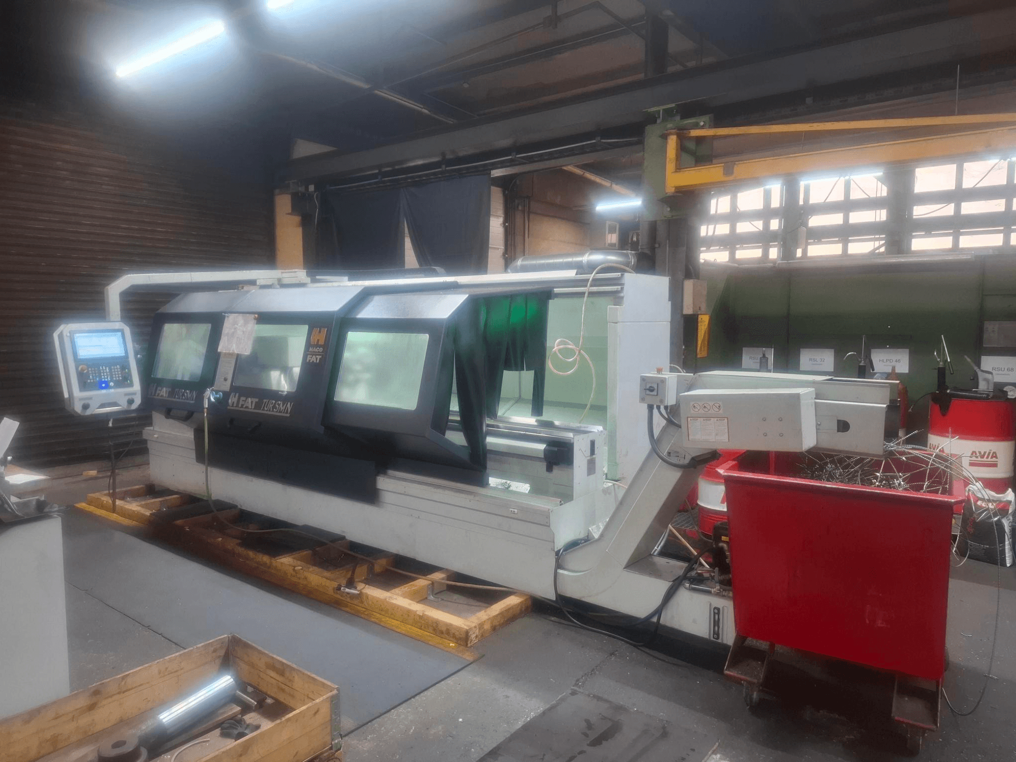 Prednji pogled na CNC stroj FAT Tursan s upravljačkom pločom, postavljen na drvenim paletama u radionici.