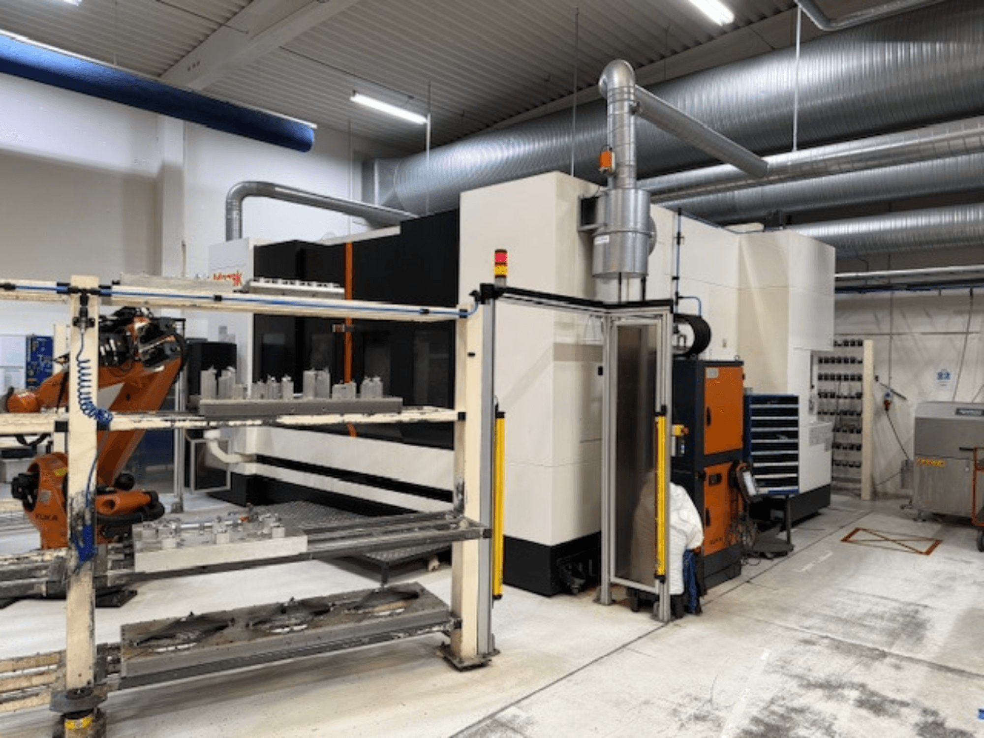 Industrijski CNC stroj s robotskom rukom i sigurnosnim barijerama, s prednjim pogledom na postavku u prozračnom radnom prostoru.