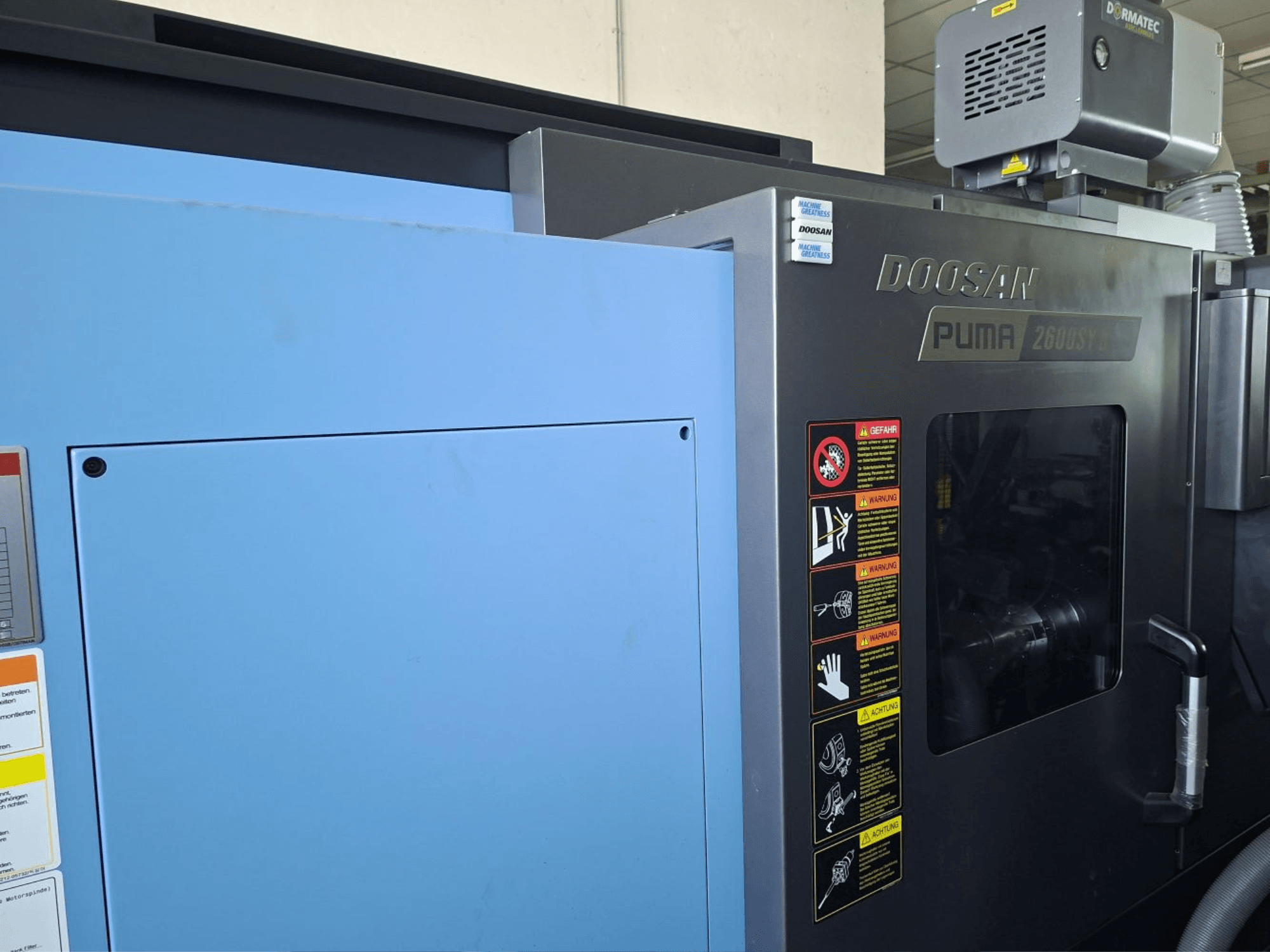 Horizontalni tokarski stroj DOOSAN PUMA 2600 SY II, prednji pogled, s oznakama sigurnosti i plavim pločama.