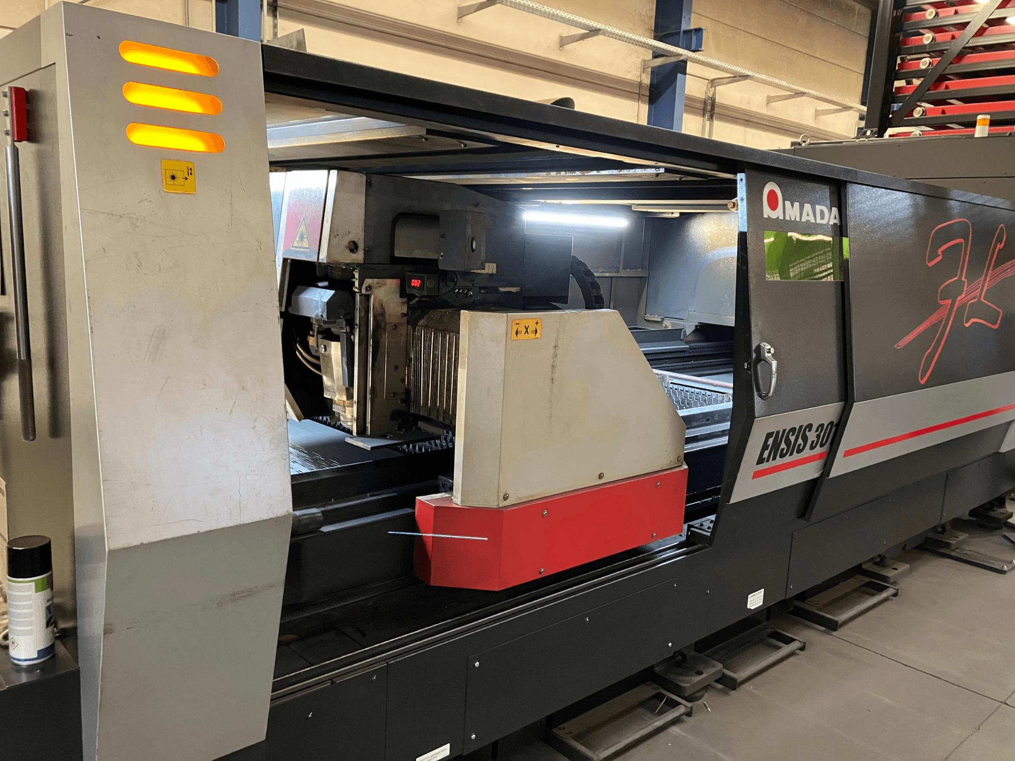 Stroj za rezanje vlaknastim laserom AMADA ENSIS 3015 AJ, prednji pogled, prikazuje glavu za rezanje i upravljačke elemente unutar metalnog okvira.