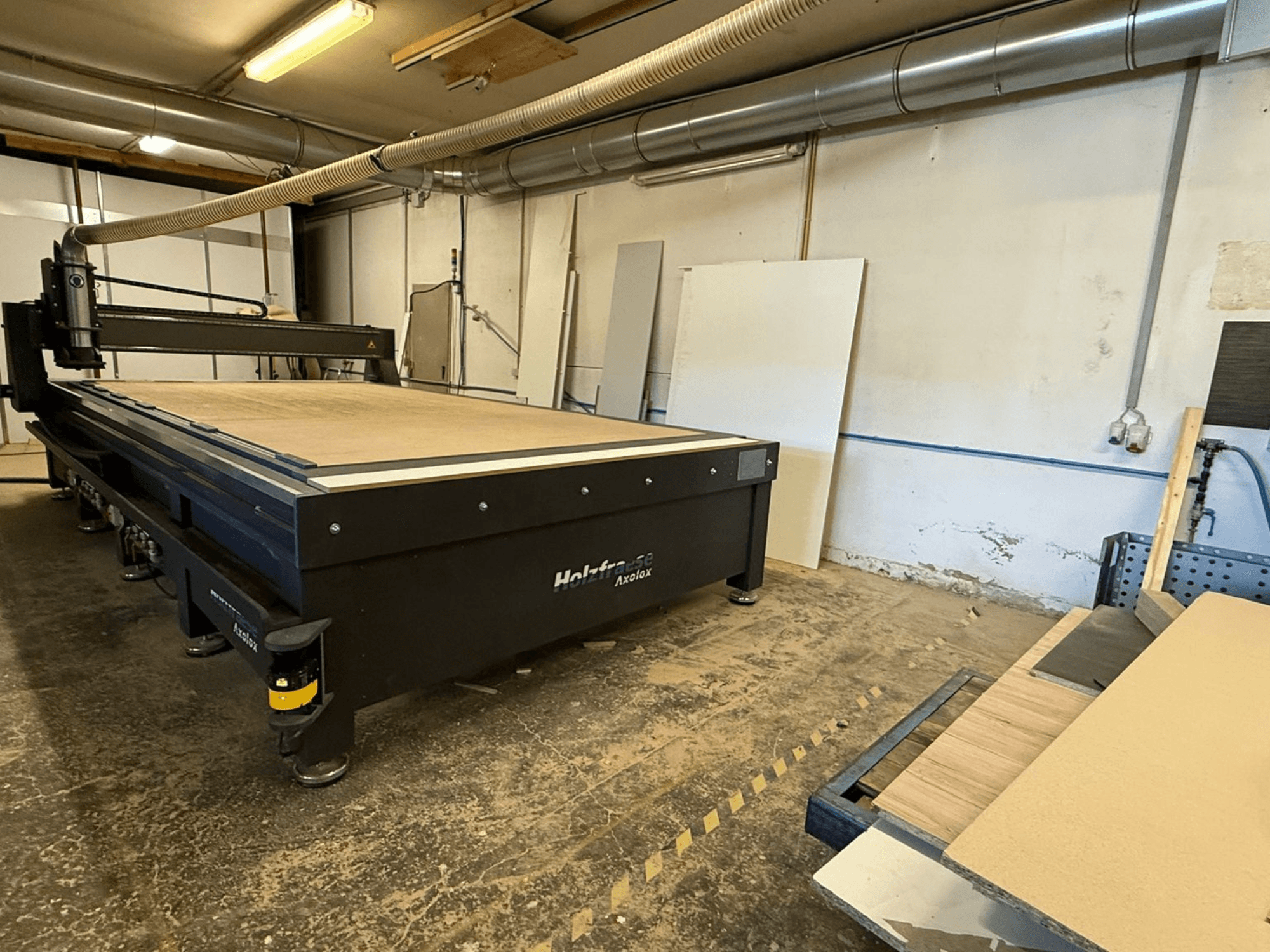 Holz-Her Axos 5 CNC glodalica u radionici, prednji pogled koji prikazuje radni stol, sustav za usisavanje prašine i drvene ploče u blizini.