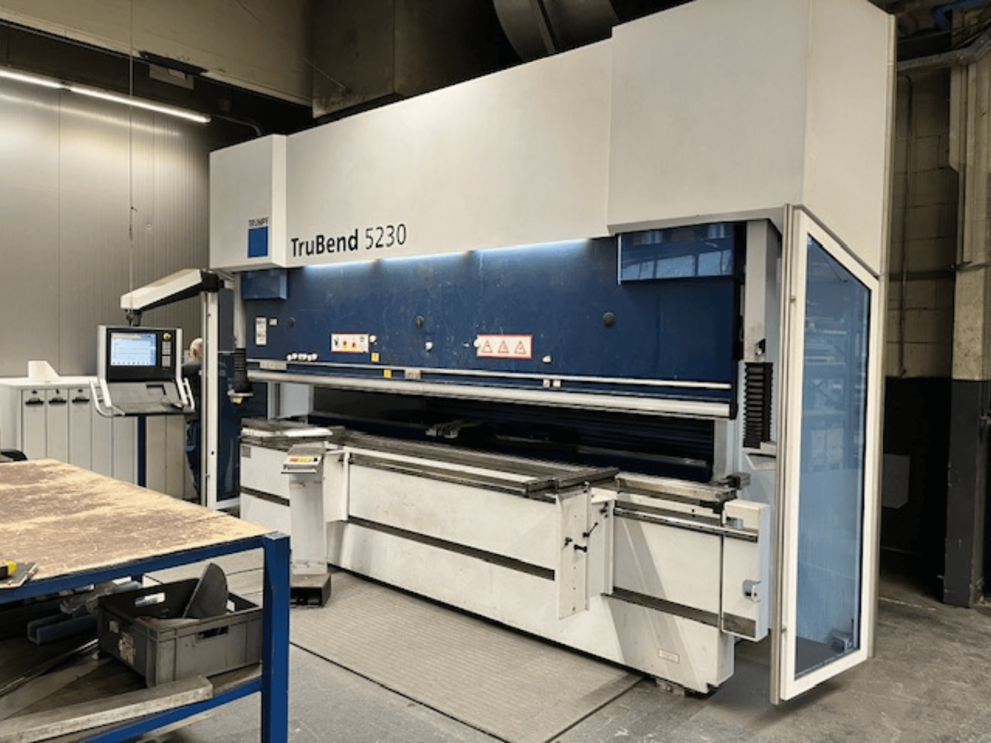 Stroj za savijanje TruBend 5230 u industrijskom okruženju; prednji pogled s upravljačkom pločom, sigurnosnim značajkama i radnim stolom.