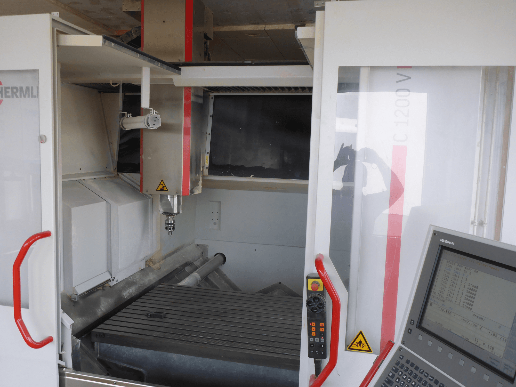 Unutrašnjost vertikalnog obradnog centra HERMLE C 1200 s prikazom držača alata, upravljačke ploče i radnog stola s prednje strane.