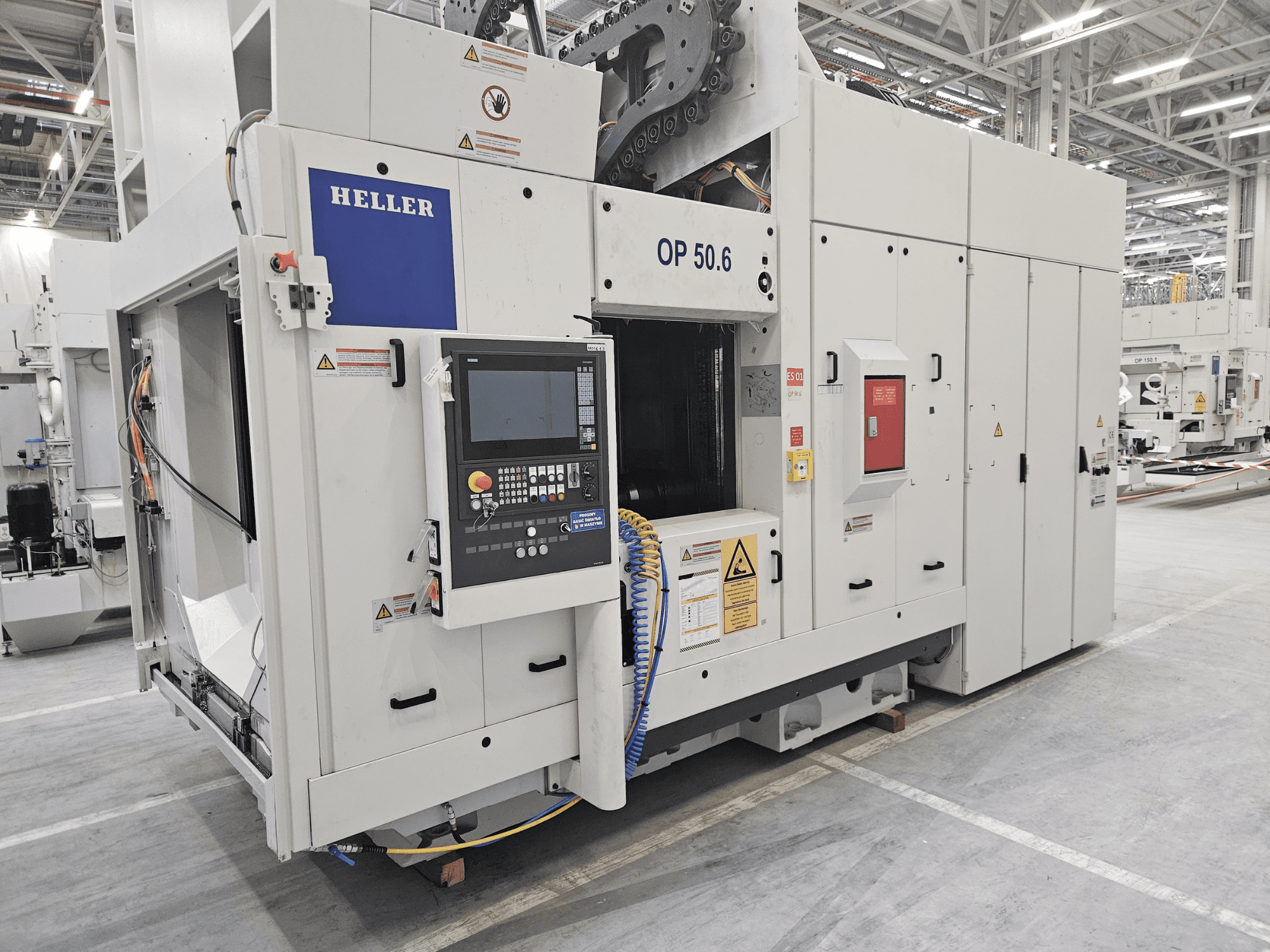 Obradni centar Heller OP 50.6, prednji pogled, s upravljačkom pločom, naljepnicama s upozorenjima i crijevima vidljivim u tvorničkom okruženju.