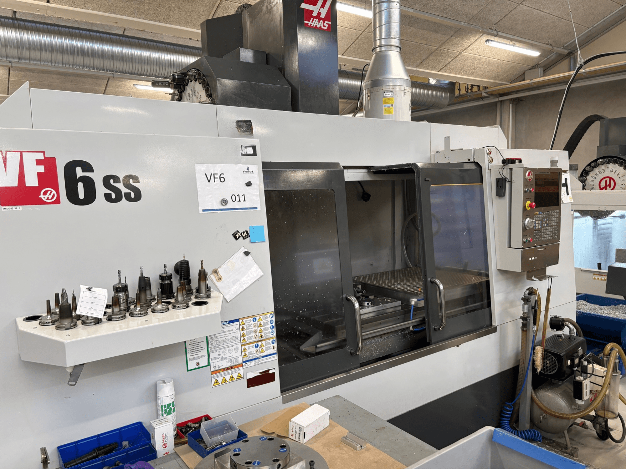 Haas VF-6 SS CNC glodalica, prednji pogled. Sadrži razne alate, upravljačku ploču i vidljivi unutarnji radni prostor.