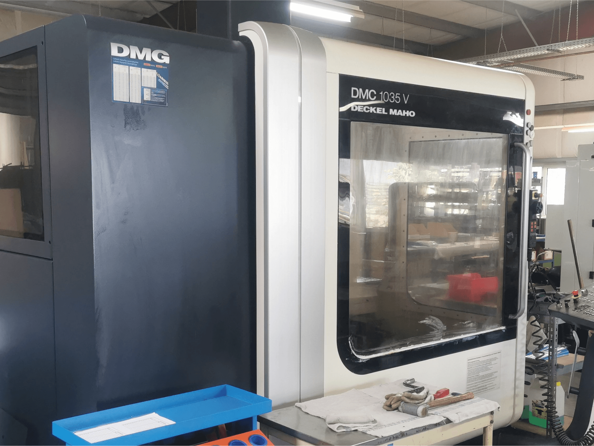 Glodalica DMG DMC 1035 V u radionici, prednji pogled s plavom ladicom za alat i rukavicama na površini.