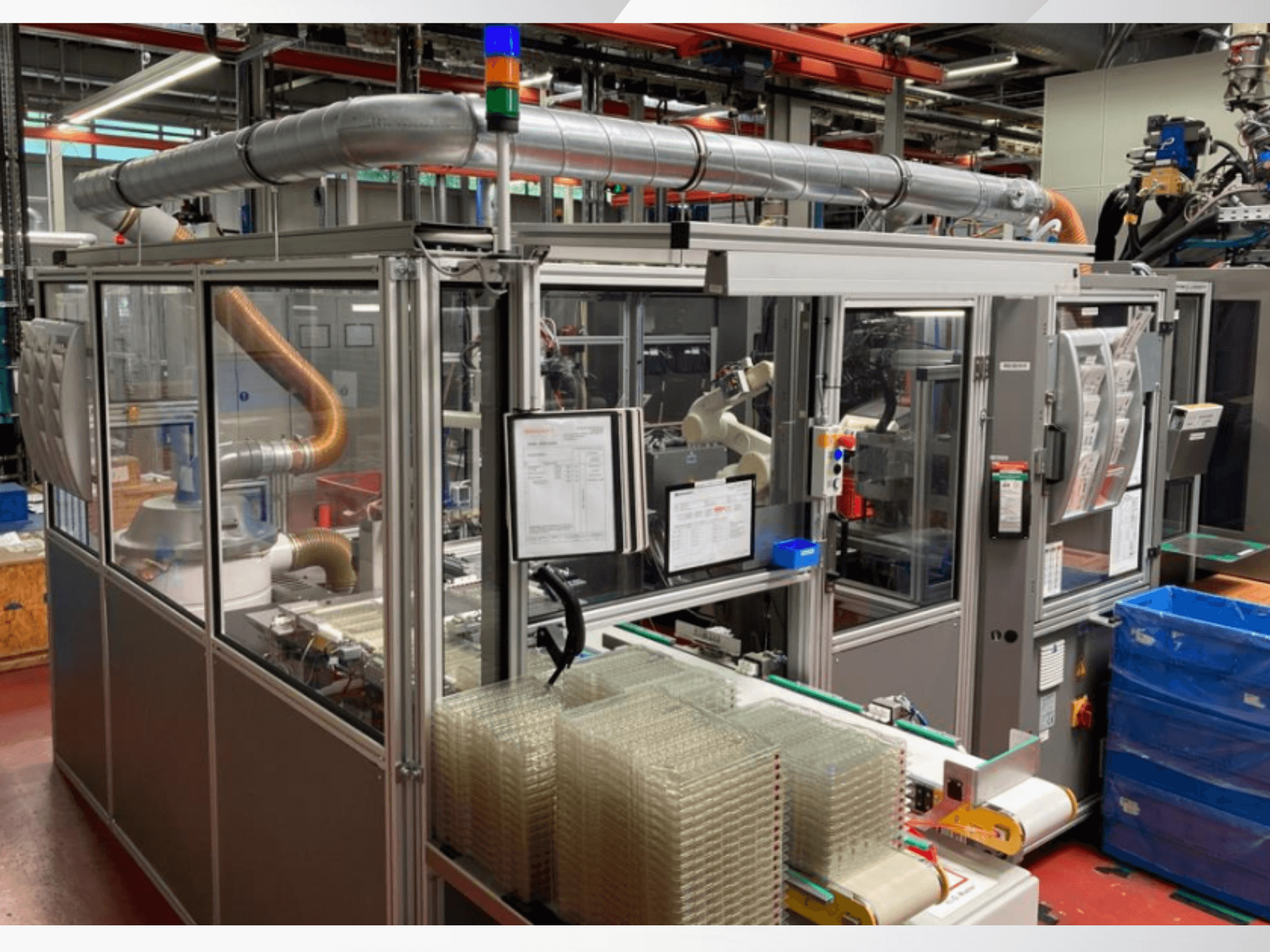 Automatizirani stroj za sastavljanje s robotskom rukom, prozirnim bočnim pločama i naslaganim spremnicima prozirnih predmeta, pogled sprijeda.