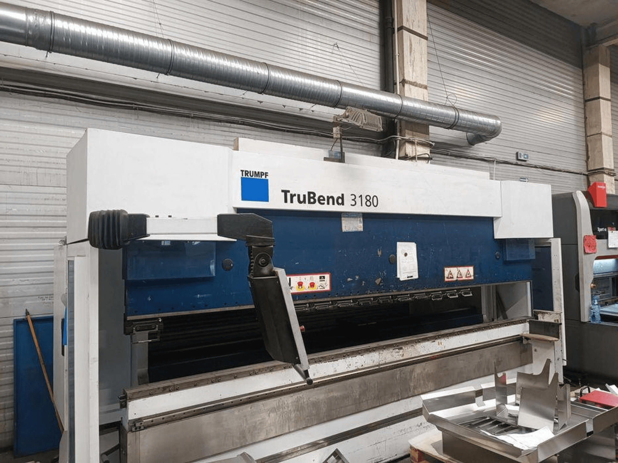 Trumpf TruBend 3180 stroj za savijanje u radionici, bočni pogled koji prikazuje upravljačku ploču i metalne dijelove na stolu.