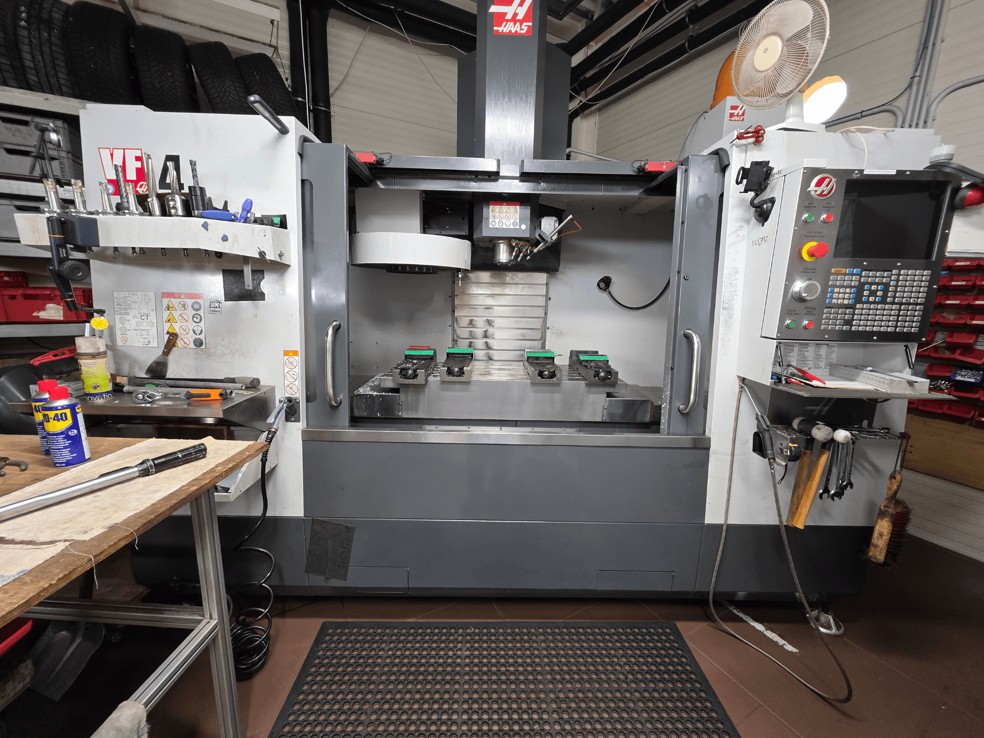 Prednji pogled na Haas VF-4 CNC glodalicu u radionici, s alatima, računalnim sučeljem i dvama obratcima na stolu.