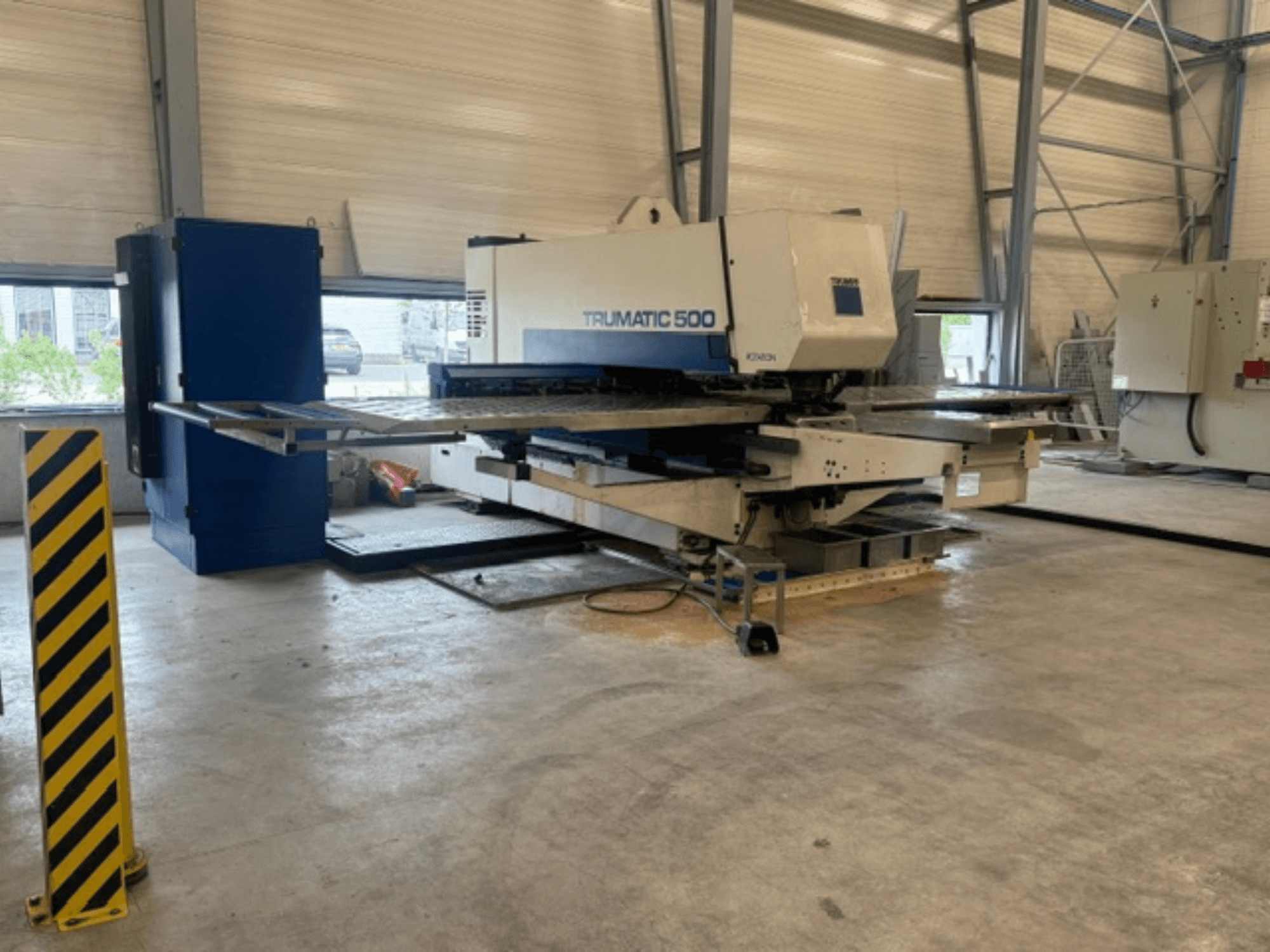 CNC stroj za probijanje TRUMPF Trumatic 500 u radionici, bočni pogled koji prikazuje strojeve i sigurnosni stup sa žutim prugama.