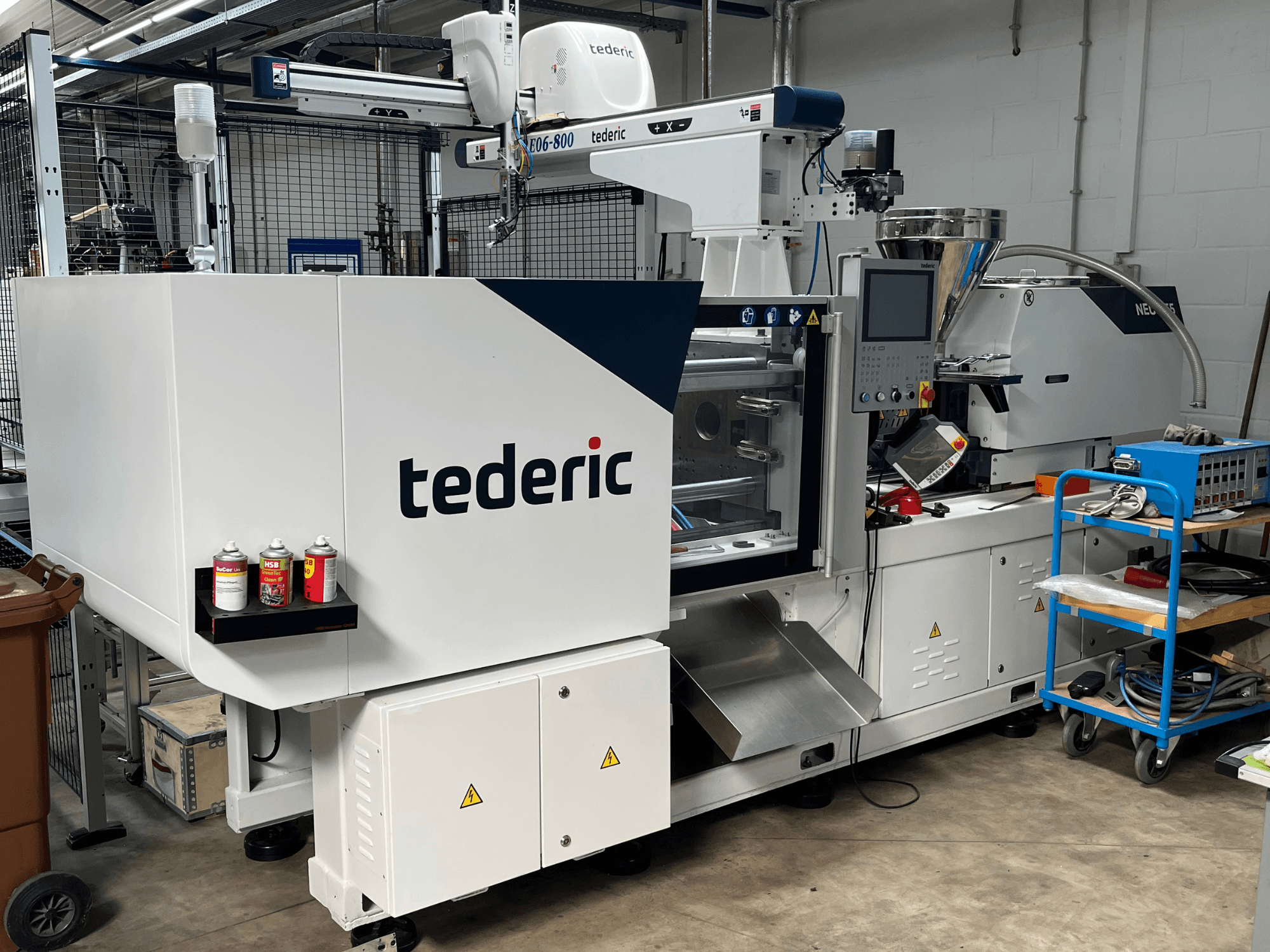 Hidraulički stroj za brizganje plastike TEDERIC NEO.E55/e110h u radionici, bočni pogled s upravljačkom pločom i susjednim alatima.