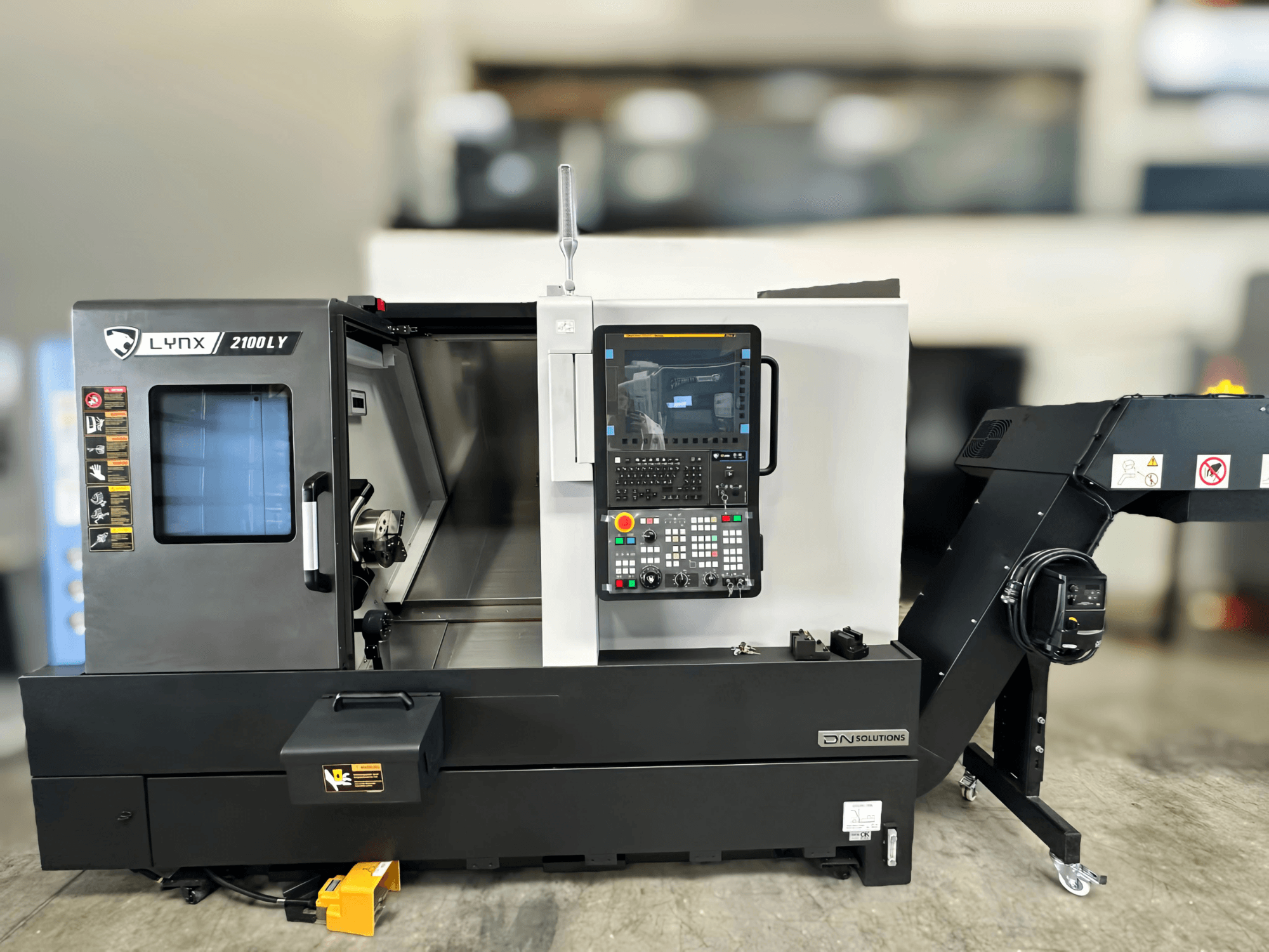 Horizontalni tokarski stroj DN SOLUTIONS LYNX 2100LYB, prednji pogled, s upravljačkom pločom i otvorenim vratima koja otkrivaju unutrašnjost.