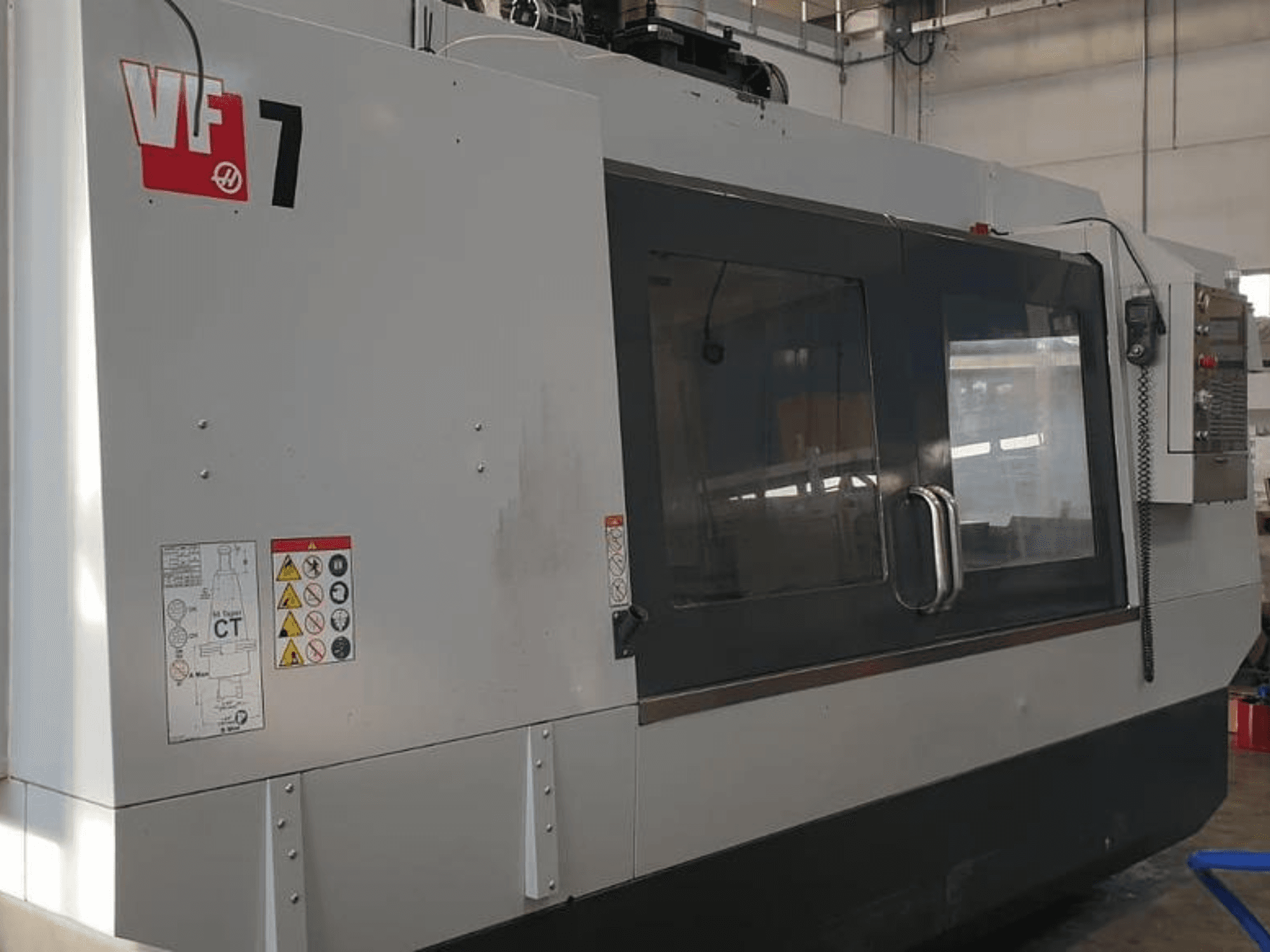 Haas VF-7 CNC stroj u bočnom pogledu, s metalno sivom završnom obradom, upravljačkom pločom i sigurnosnim naljepnicama.