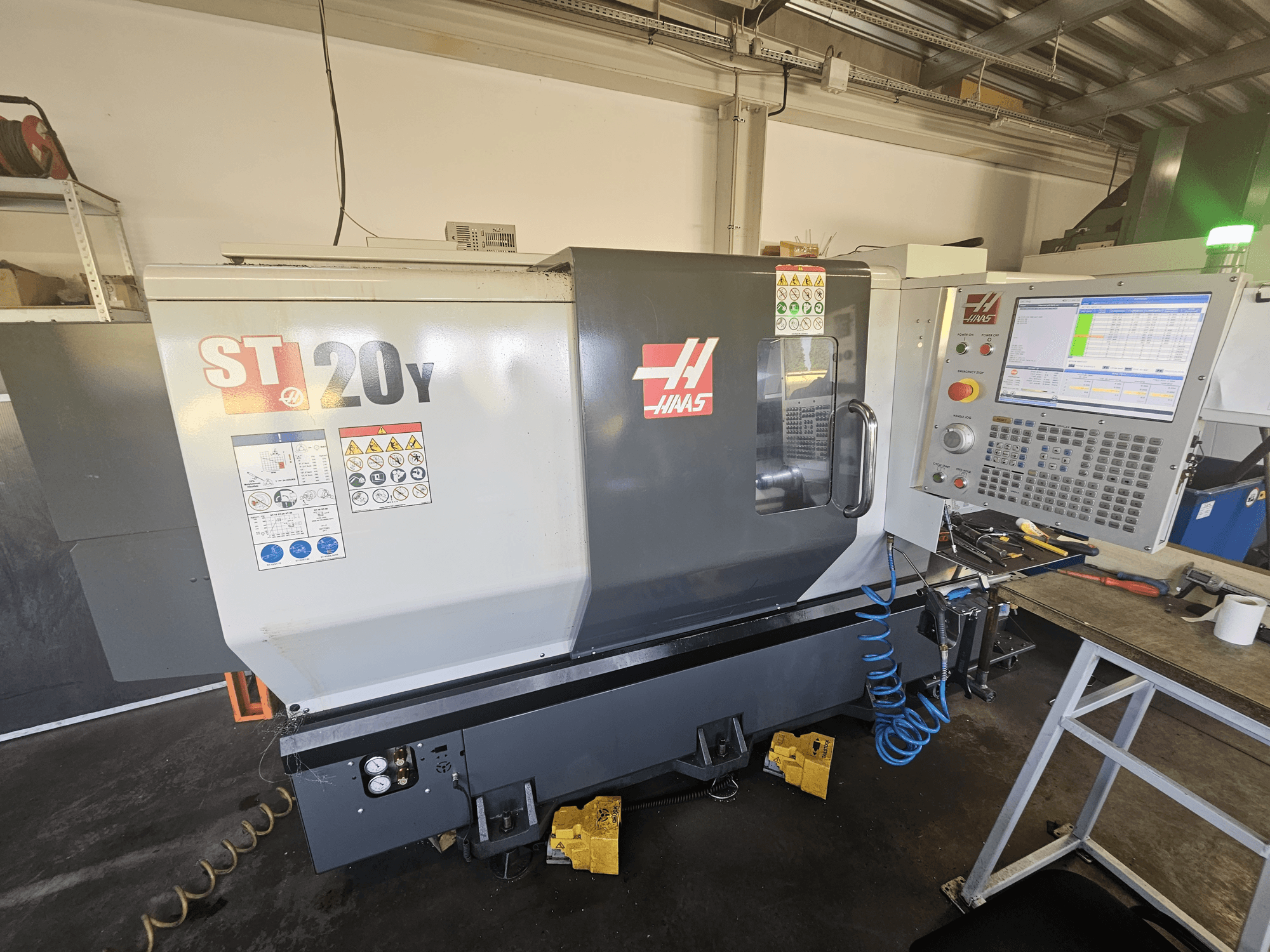 Haas ST-20Y CNC tokarilica s prednje strane s upravljačkom pločom; uključuje sigurnosne naljepnice i detalje crijeva za zrak sa strane.
