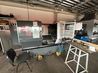 Haas CNC tokarilica (model ST-10) u radionici, bočni pogled s upravljačkim elementima, alatima na radnom stolu i stolicom u blizini.