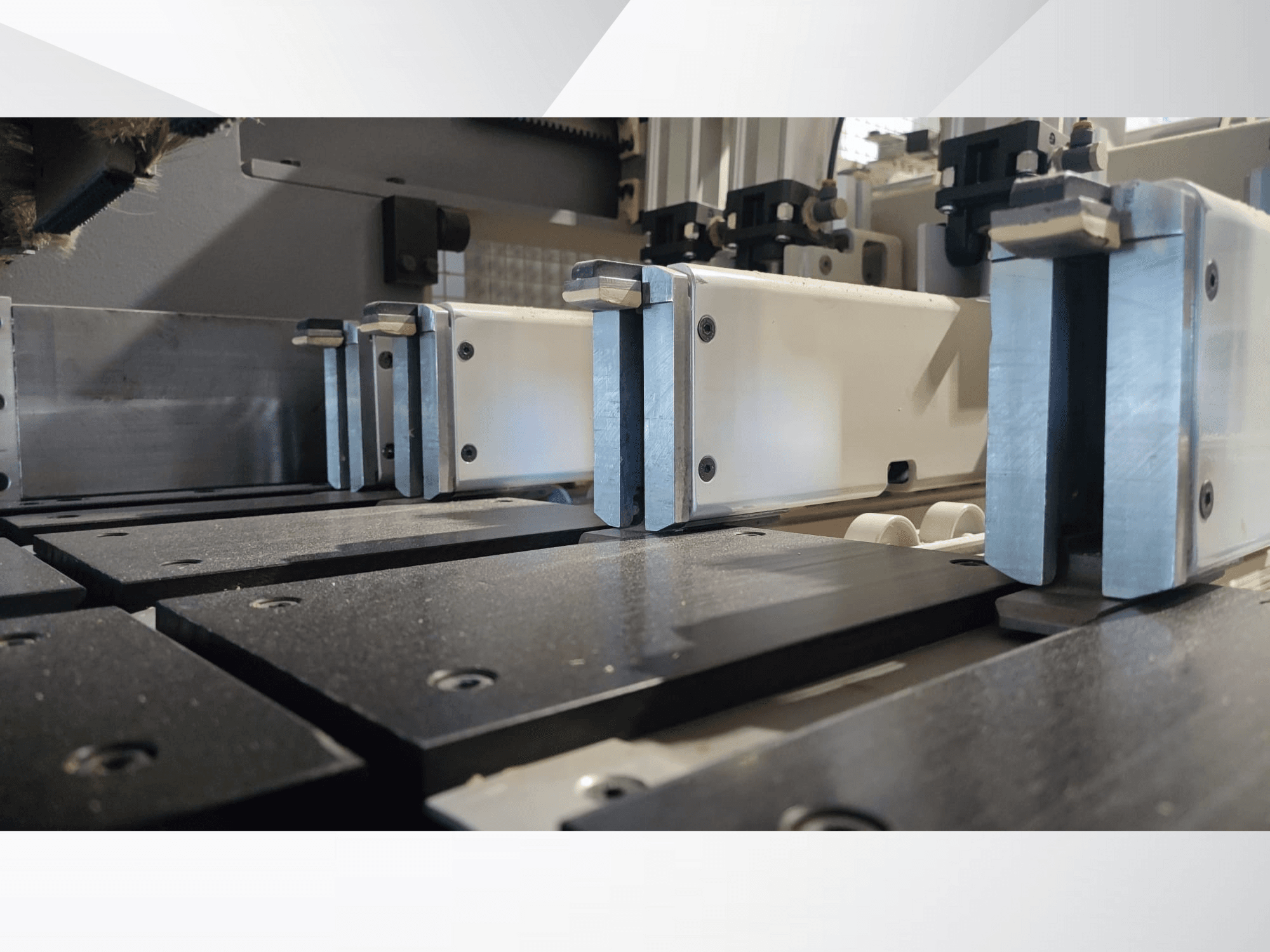 Pogled izbliza na stezni mehanizam preciznog stroja s metalnim čeljustima, s crnim radnim površinama i vidljivim vodećim tračnicama.