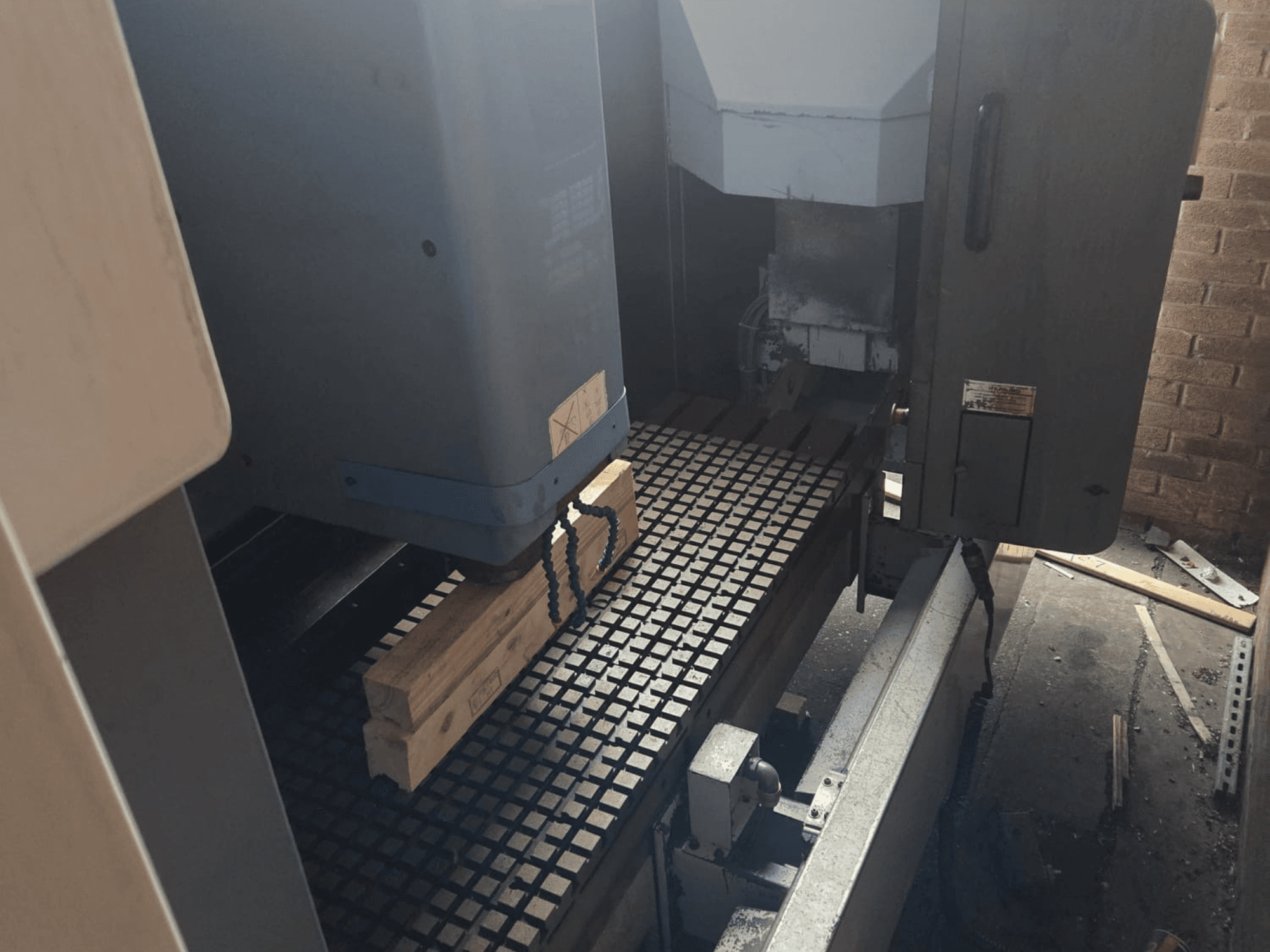 Prednji pogled na CNC stroj s drvenim daskama na rešetkastom stolu, s alatima i kontrolama sa strane.