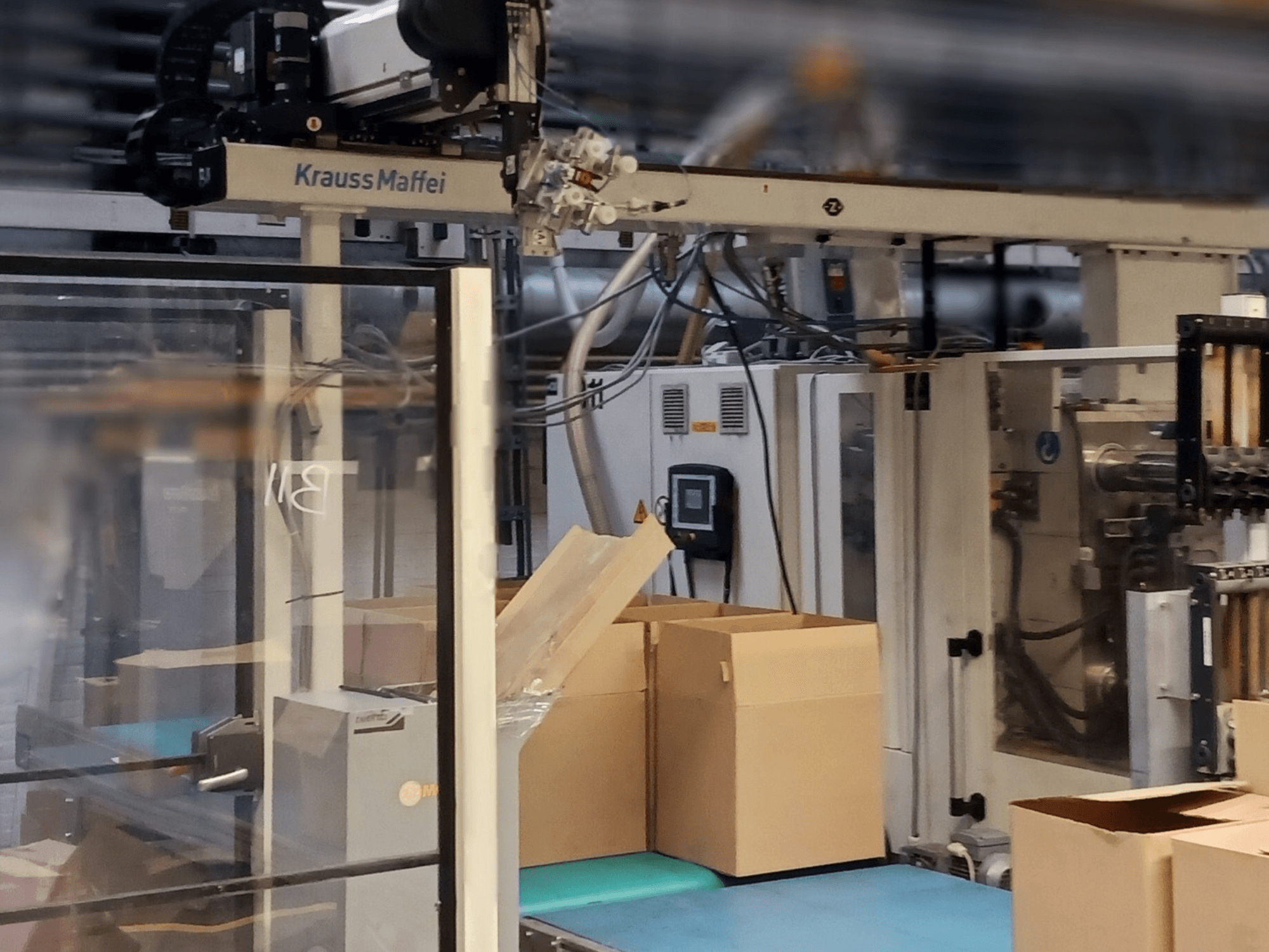 Krauss Maffei automatizacijski sustav u tvornici, prednji pogled koji prikazuje kutije na transporteru i komponente strojeva u radu.