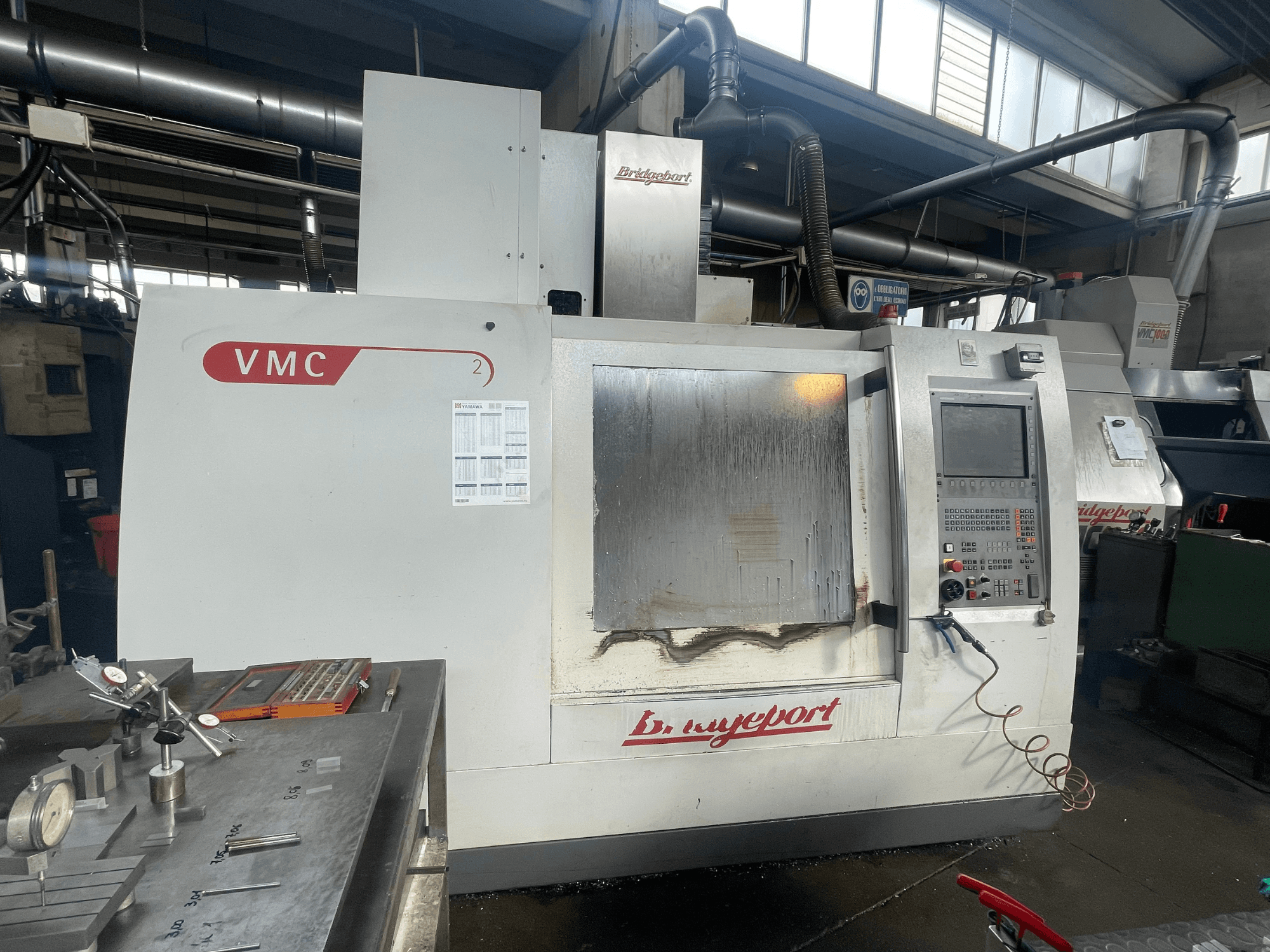 Vertikalni obradni centar Bridgeport VCM 800-30 u radionici, s upravljačkom pločom i stolom za alate. Prednji pogled s vidljivim detaljima.