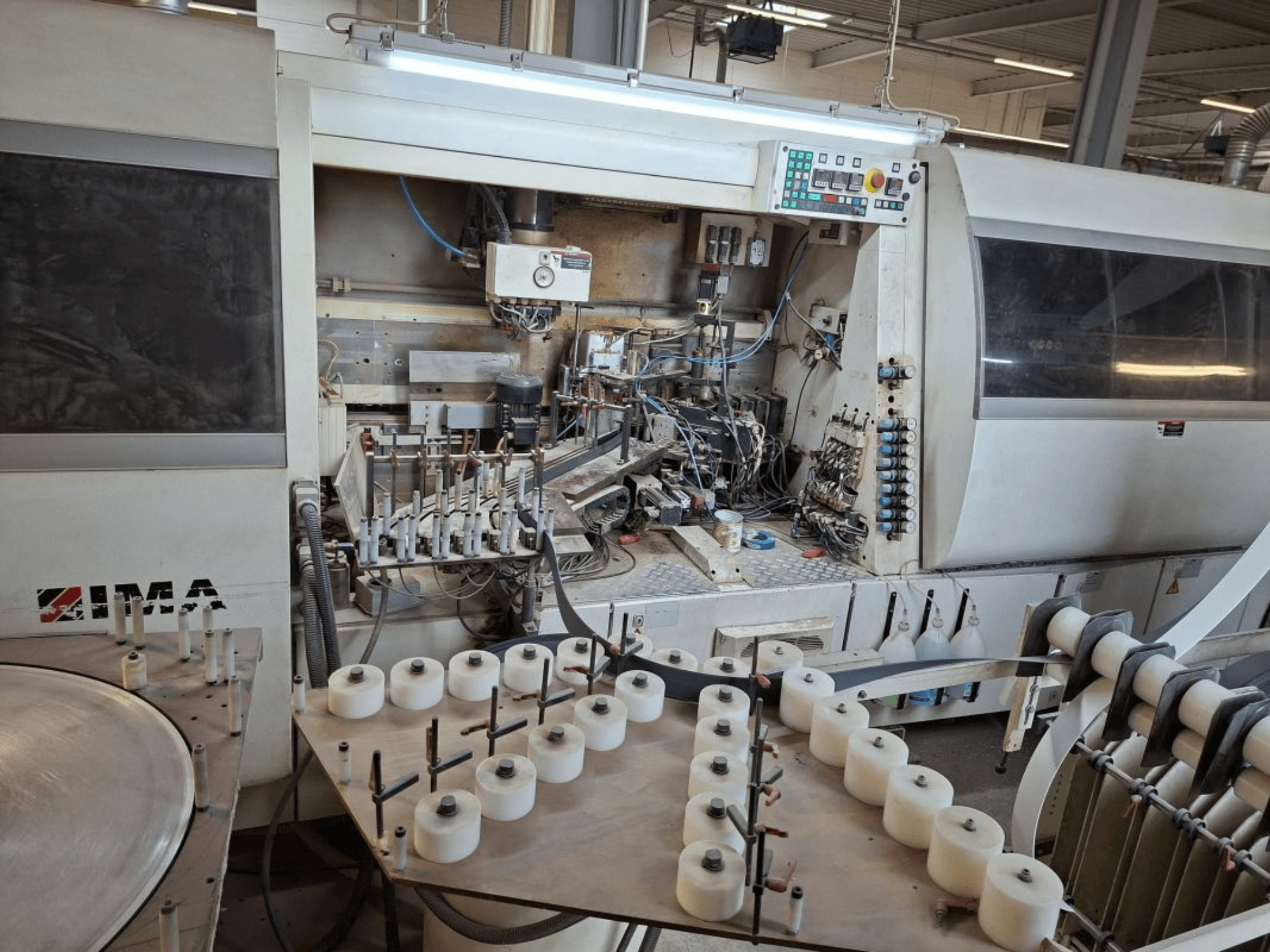 IMA strojevi gledani sa strane, s prikazom složenih mehaničkih komponenti i okruglog stola s bijelim kalemovima.