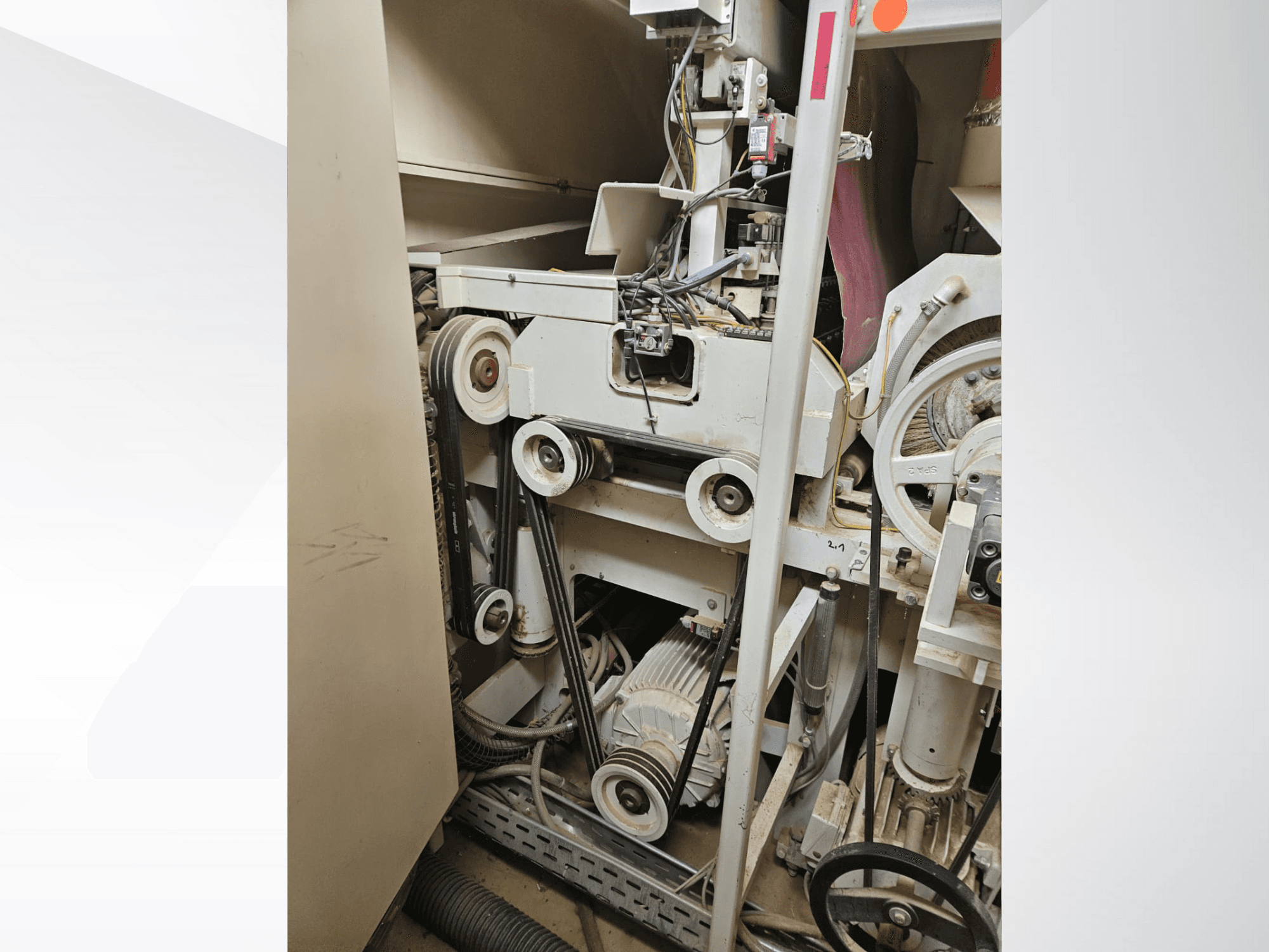 Unutrašnjost industrijskog stroja s remenima i remenicama, s motorom i ožičenjem, gledano sa strane.