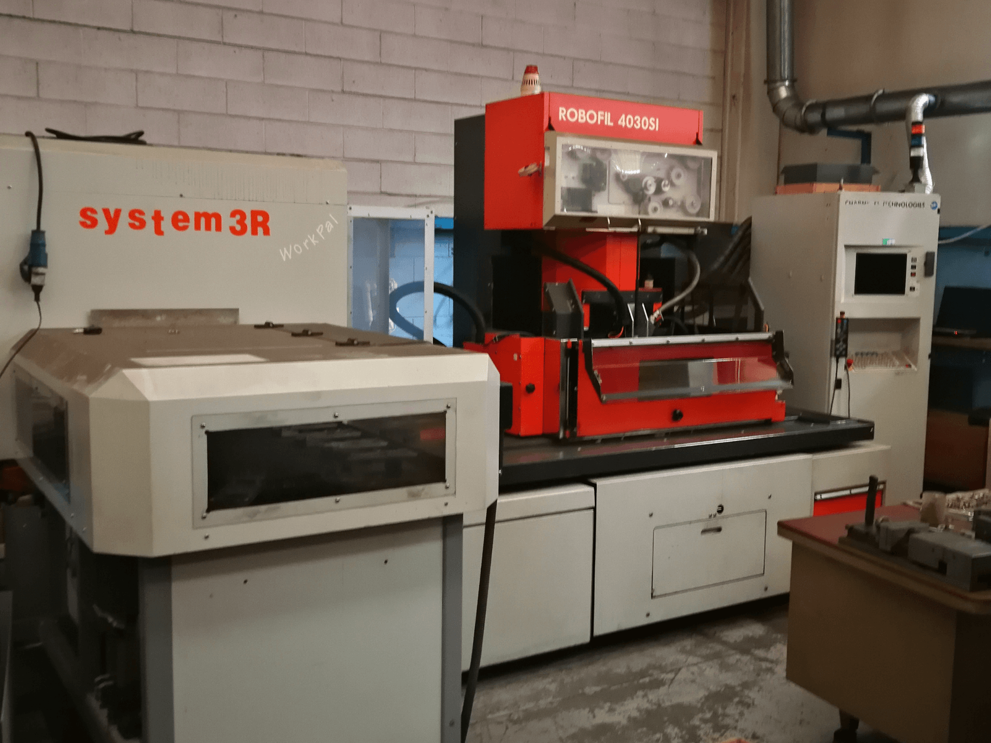 Prednji pogled na stroj za žičanu eroziju CHARMILLES ROBOFIL 4030 Si, s crvenom i sivom vanjštinom i susjednom radnom stanicom system3R.
