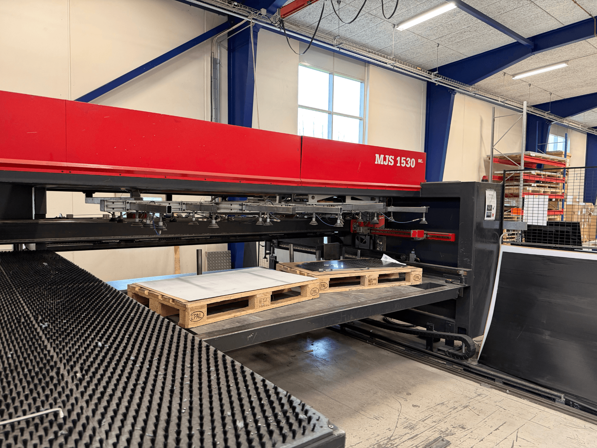 CNC stroj MJS 1530 u radionici, prednji pogled, s drvenom paletom koja drži metalni lim na podignutoj platformi.