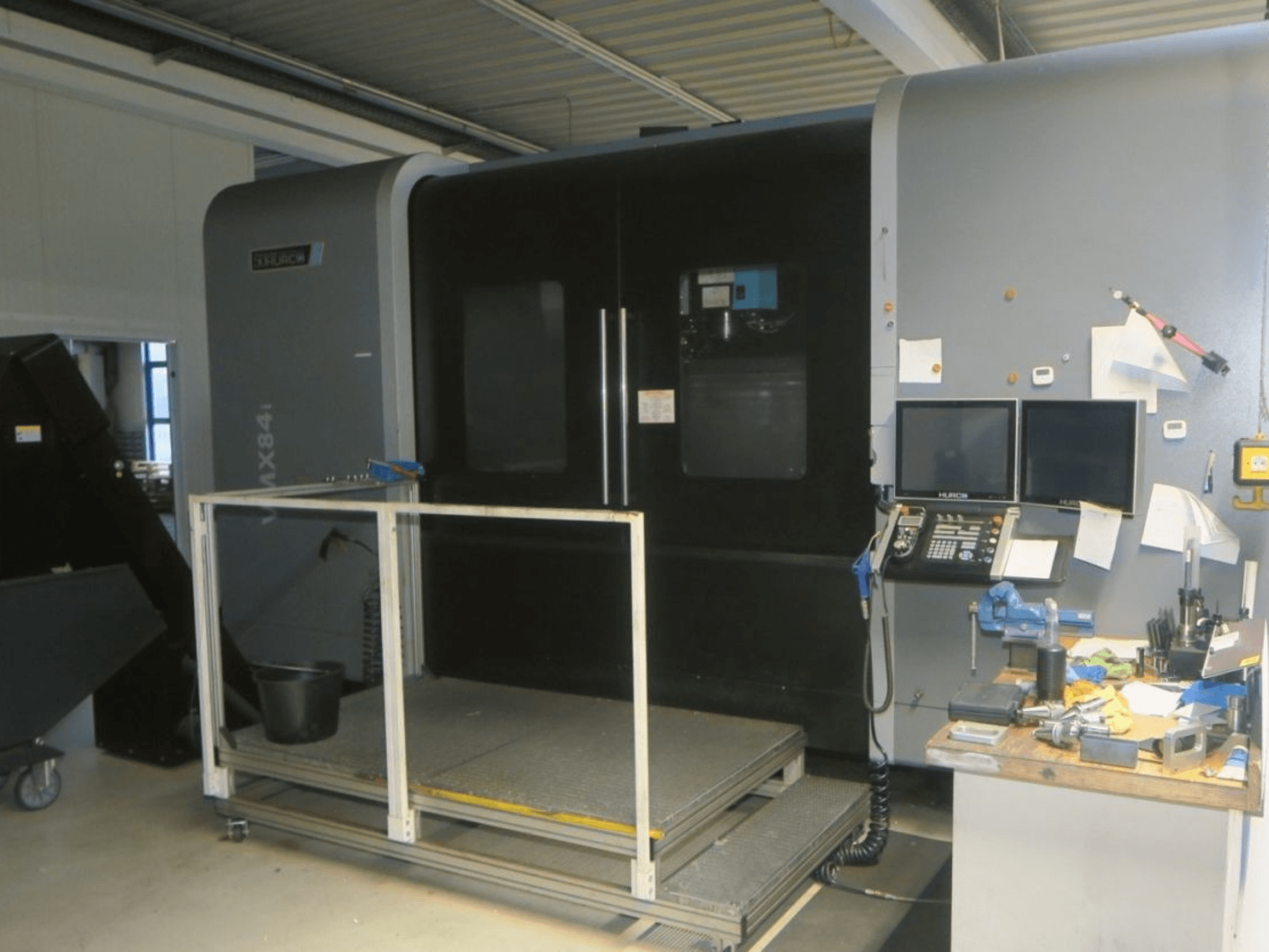 Hurco MX84 CNC stroj u prednjem pogledu, s dva monitora, upravljačkom pločom i radnim prostorom alata s raznim alatima.
