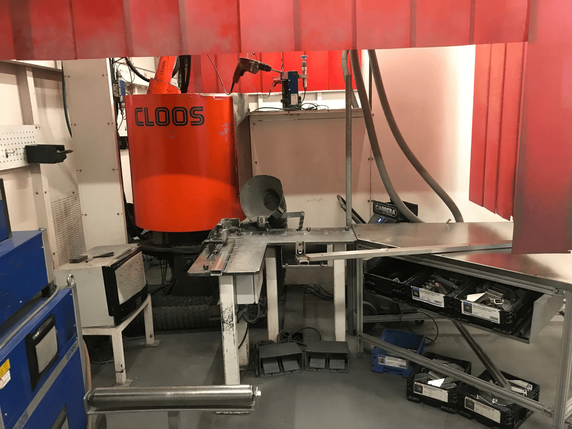 Sustav za zavarivanje tvrtke DESSAUER, prednji pogled koji prikazuje robotsku ruku, površinu za obradu metala i skladišne prostore u okruženju radionice.