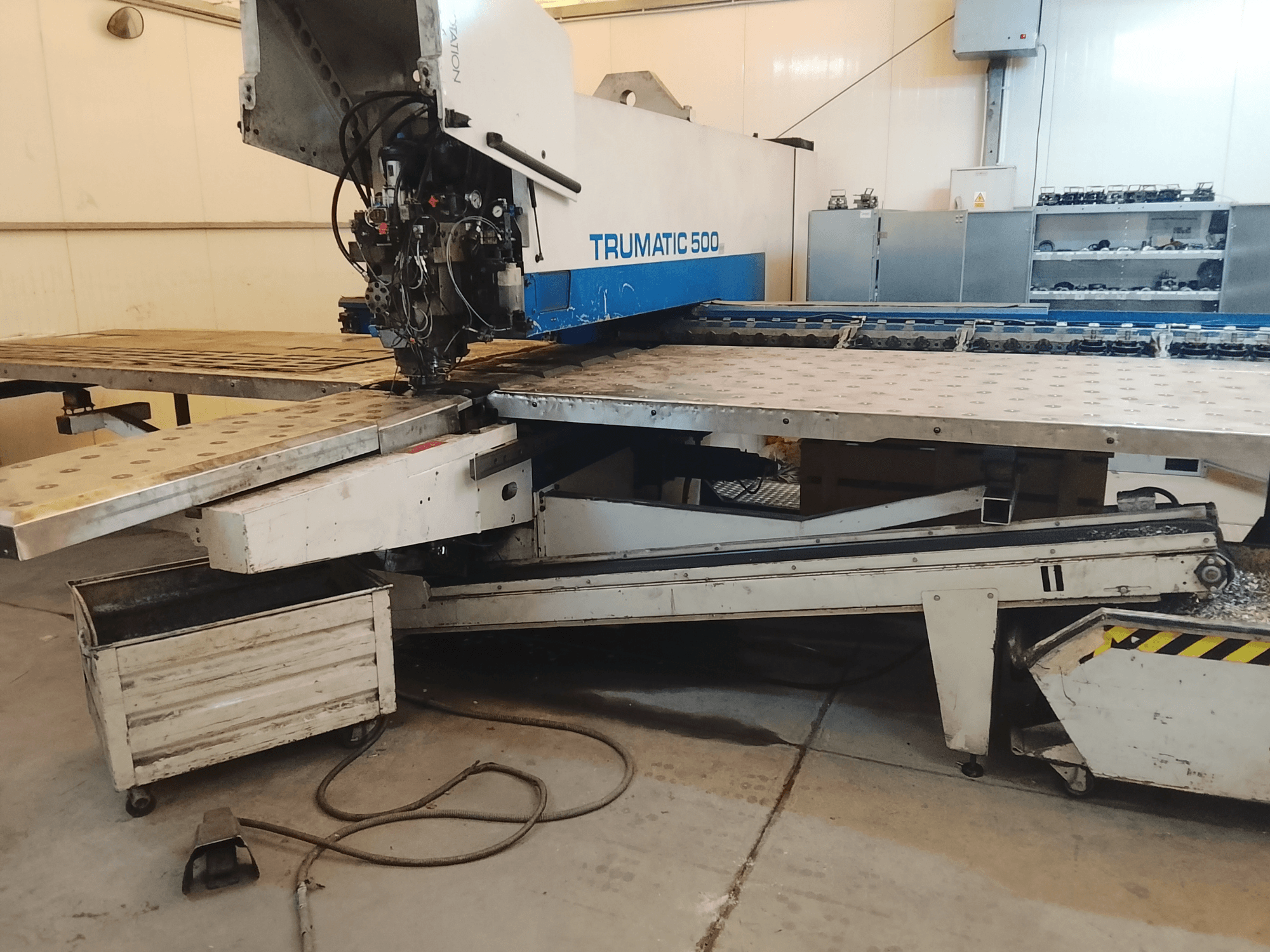 TRUMATIC 500 CNC stroj u radionici, bočni pogled koji prikazuje reznu glavu i metalni radni stol s prethodno izbušenim rupama.