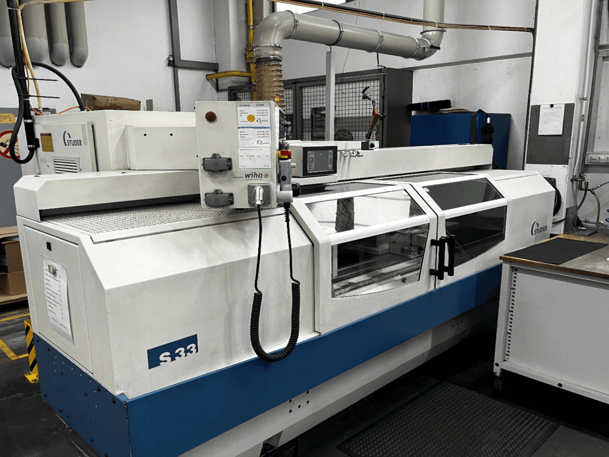 STUDER S33 CNC cilindrična brusilica, prednji pogled; ima upravljačku ploču i sigurnosna staklena vrata. Industrijsko okruženje.
