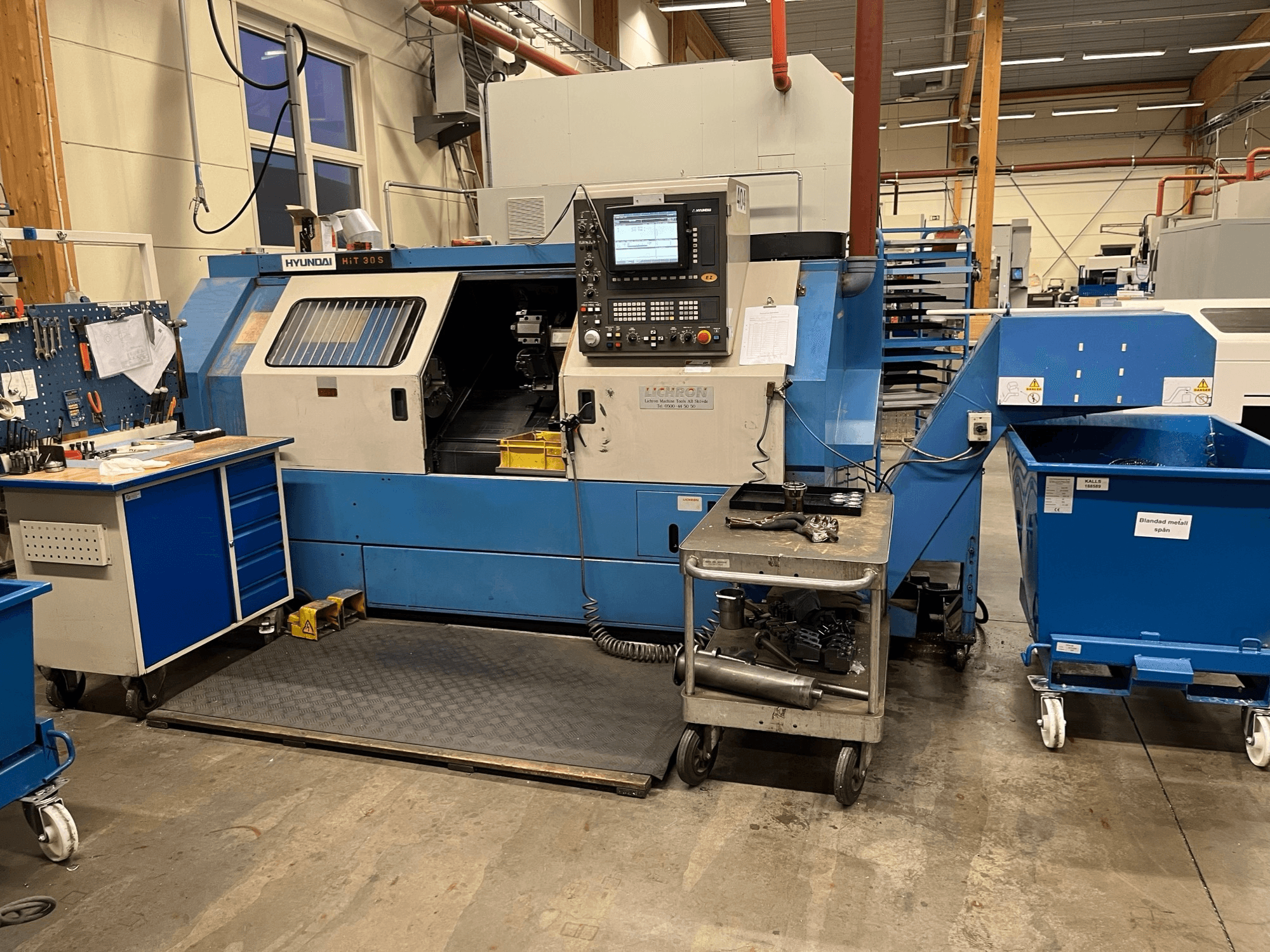 Horizontalni tokarski stroj Hyundai HIT 30S, prednji pogled, s upravljačkom pločom i alatima na obližnjim kolicima u radioničkom okruženju.