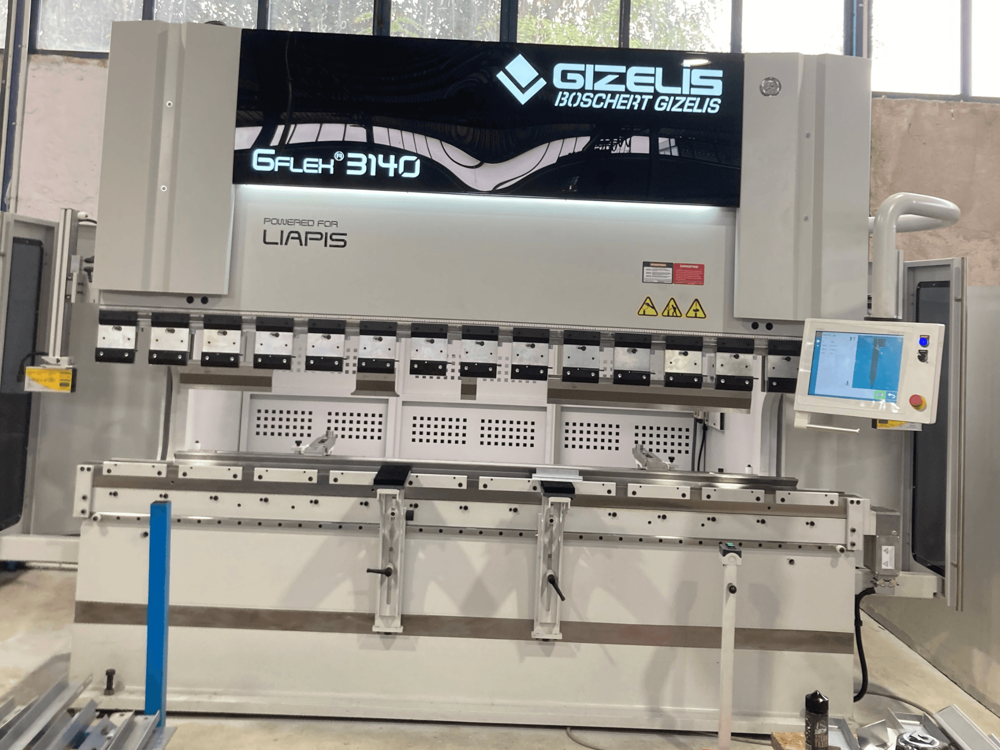 Hidraulična preša GIZELIS G-FLEX 3140 u prednjem pogledu s upravljačkim zaslonom, s više alata za savijanje i sigurnosnim naljepnicama.