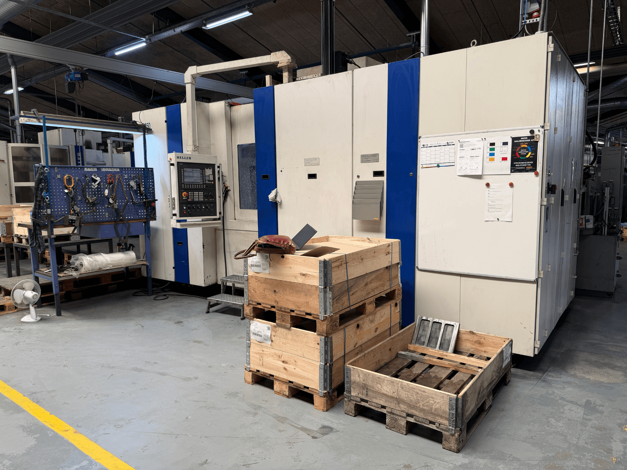 HORIZONTALNI OBRADNIČKI CENTAR HELLER MCH 250 u radionici, bočni pogled s vidljivim drvenim paletama i stalkom za alat.