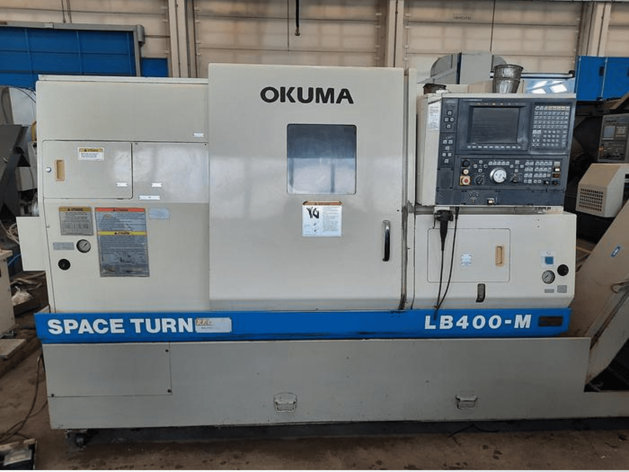 Okuma LB400-M CNC tokarski stroj, prednji pogled s upravljačkom pločom, naljepnicama s upozorenjima i vidljivim plavim natpisom "SPACE TURN".