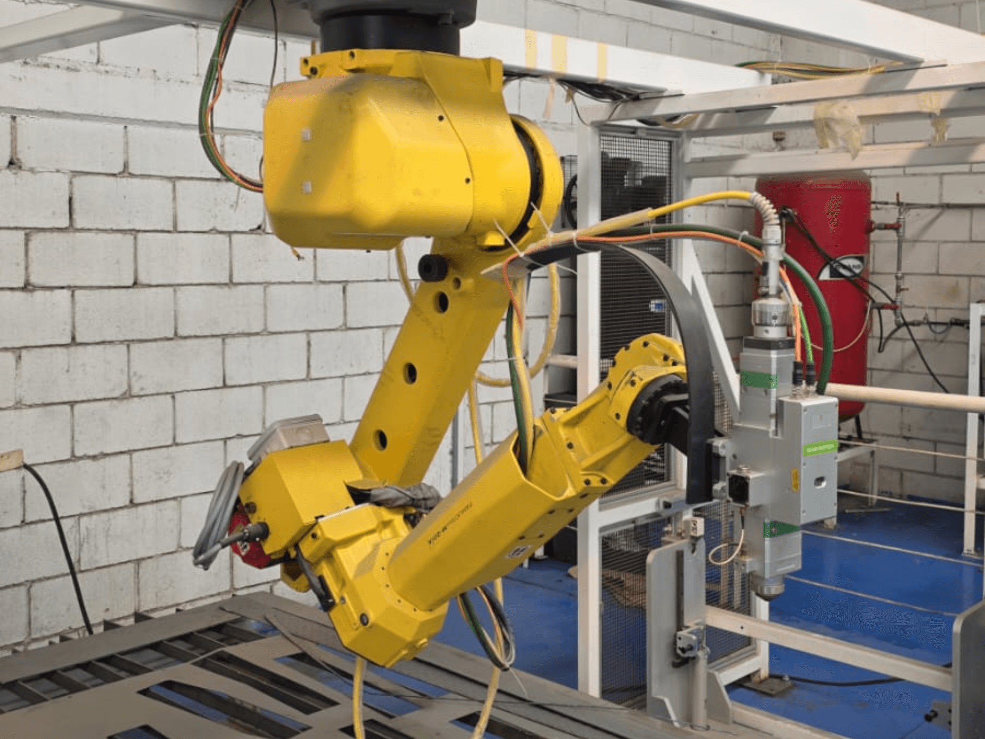Žuta robotska ruka s preciznim alatom, s više zglobova i kabela, gledana iz prednjeg kuta u industrijskom okruženju.