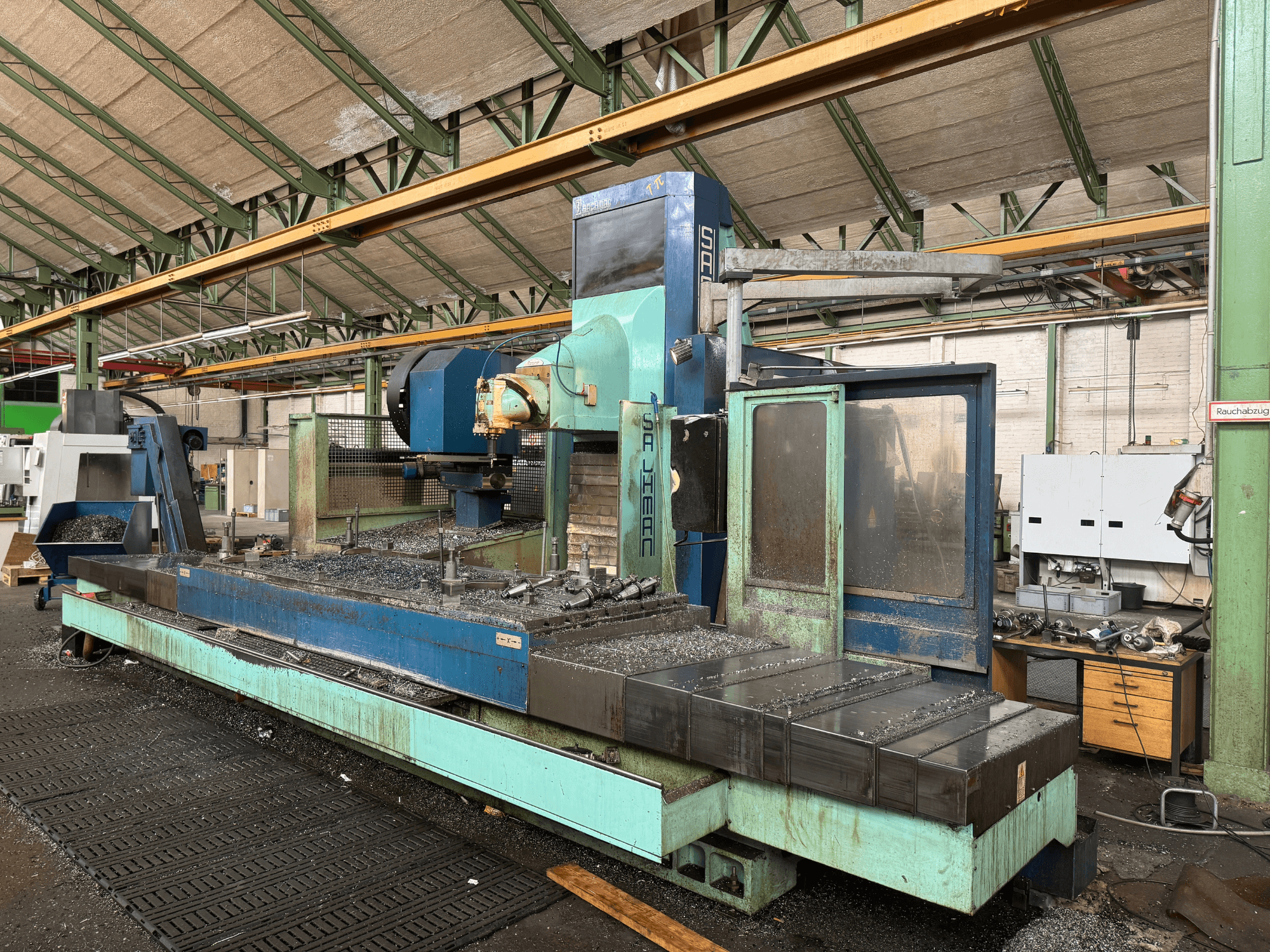 Glodalica Salvador u tvorničkom okruženju, prednji pogled, s plavo-zelenom shemom boja, s metalnim strugotinama na krevetu.