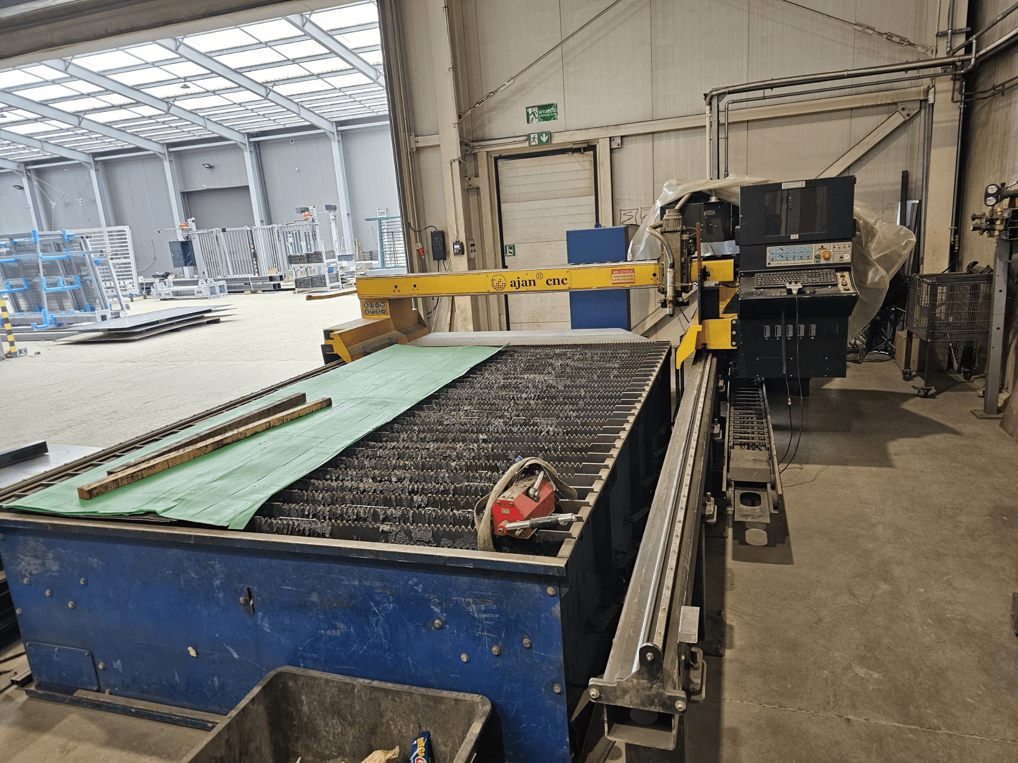 AJAN PP16011 Automatski stroj za plazma rezanje u bočnom pogledu, sa stolom za rezanje i upravljačkom pločom, smješten u radioničkom okruženju.