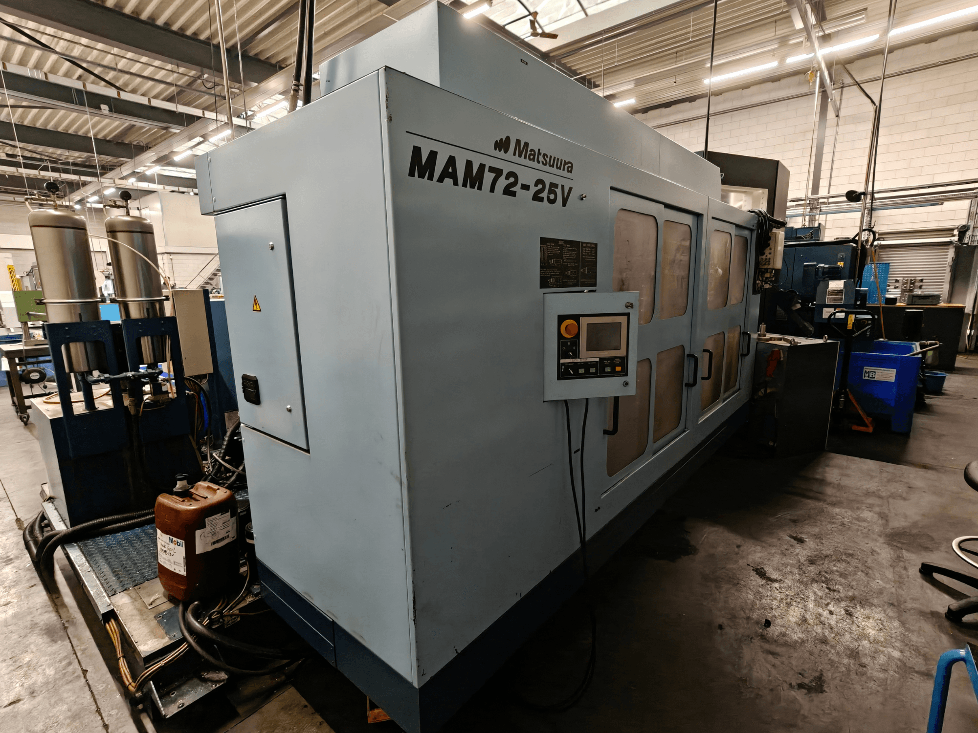 Matsuura MAM72-25V CNC stroj, bočni pogled, ima upravljačku ploču, dvostruke spremnike rashladne tekućine i radni prostor u industrijskom okruženju.