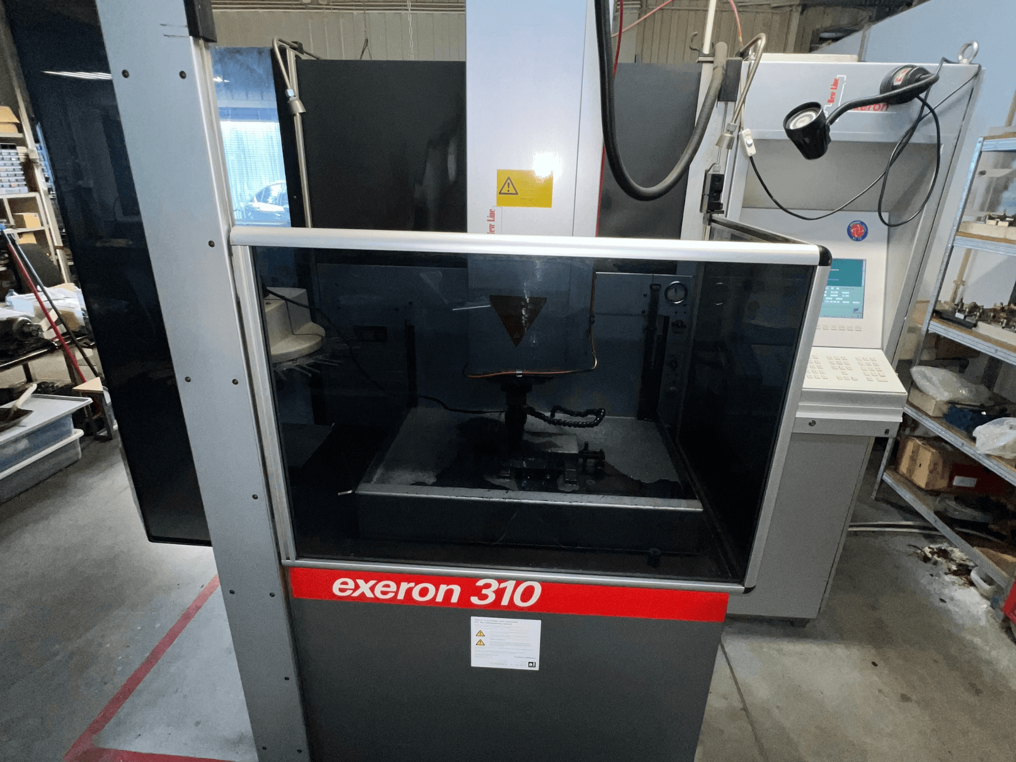 Prednji pogled na stroj Exeron 310, s prikazom staklene komore i upravljačke ploče uz police radne stanice.