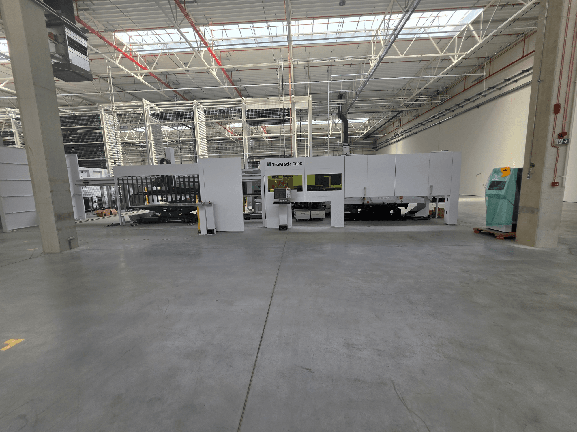 Kombinirani stroj za bušenje vlaknima i lasersko rezanje TRUMPF TruMatic 6000-1600 u prostranom skladištu, pogled sprijeda.