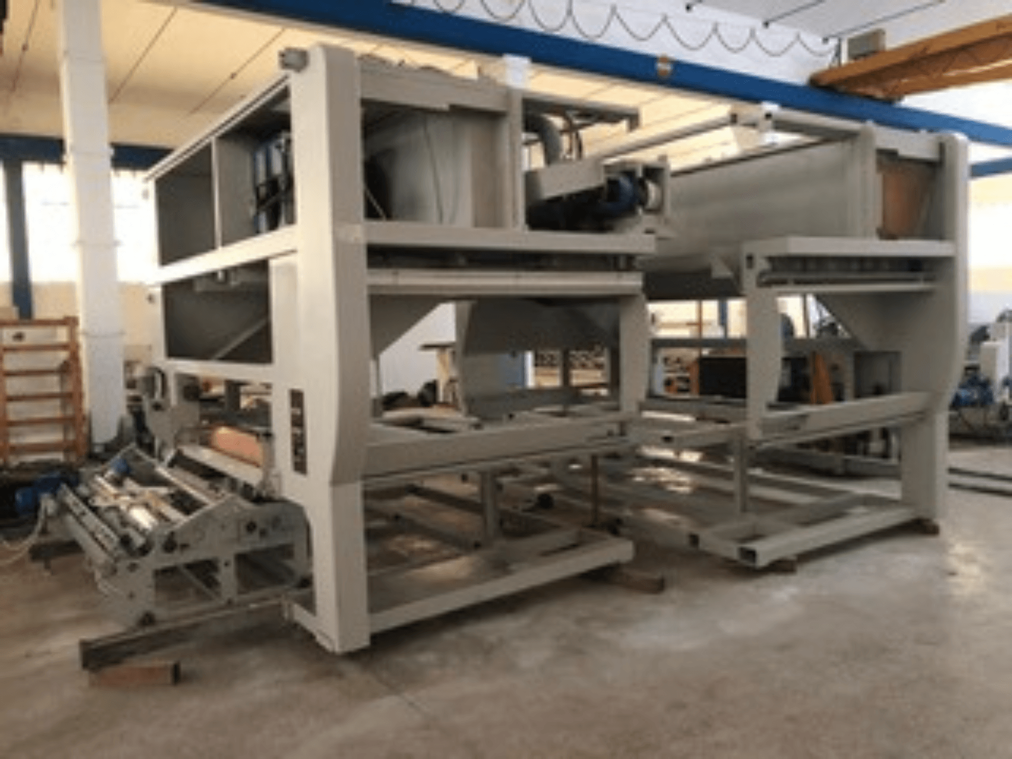 Industrijski stroj s više transportnih valjaka i velikom strukturom; bočni pogled, siva boja, smješten u dobro osvijetljenoj tvornici.