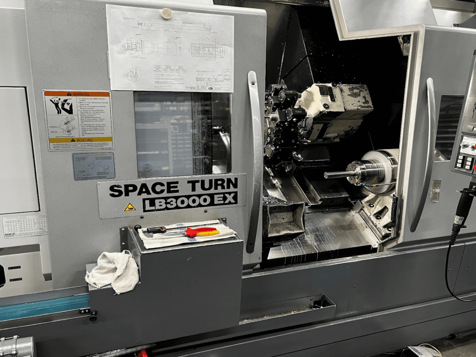 Horizontalni tokarski stroj Okuma LB3000EX MYW, prednji pogled s vidljivim upravljačkom pločom, alatima i detaljima radnog prostora.