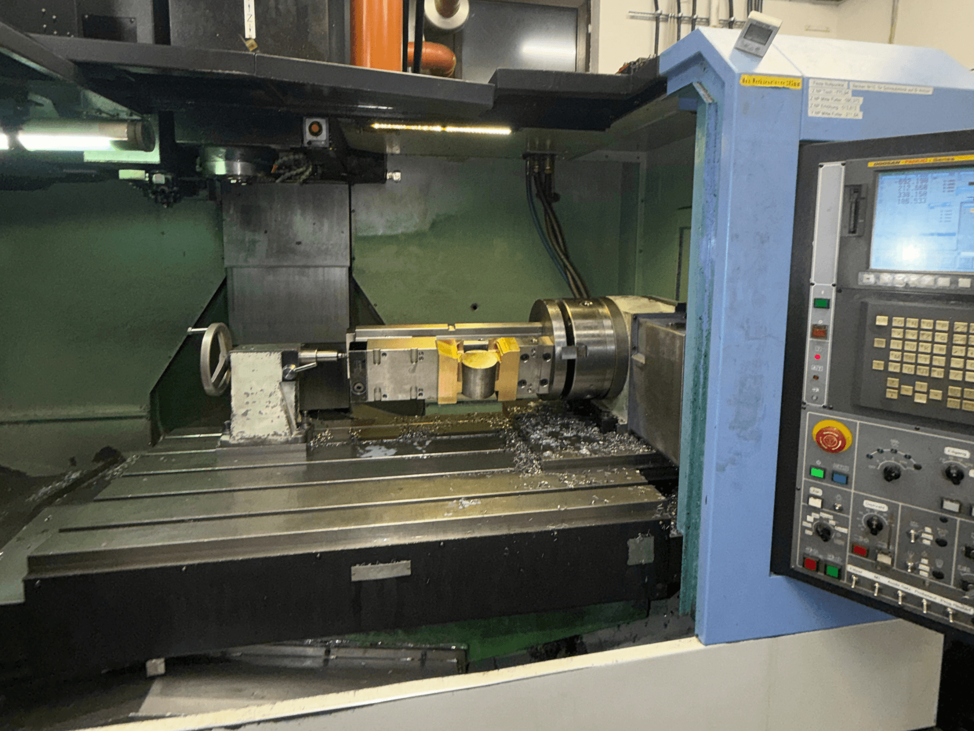 Vertikalni obradni centar DOOSAN DNM650, prednji pogled, prikazuje alat za rezanje i upravljačku ploču, s vidljivim metalnim strugotinama na stolu.